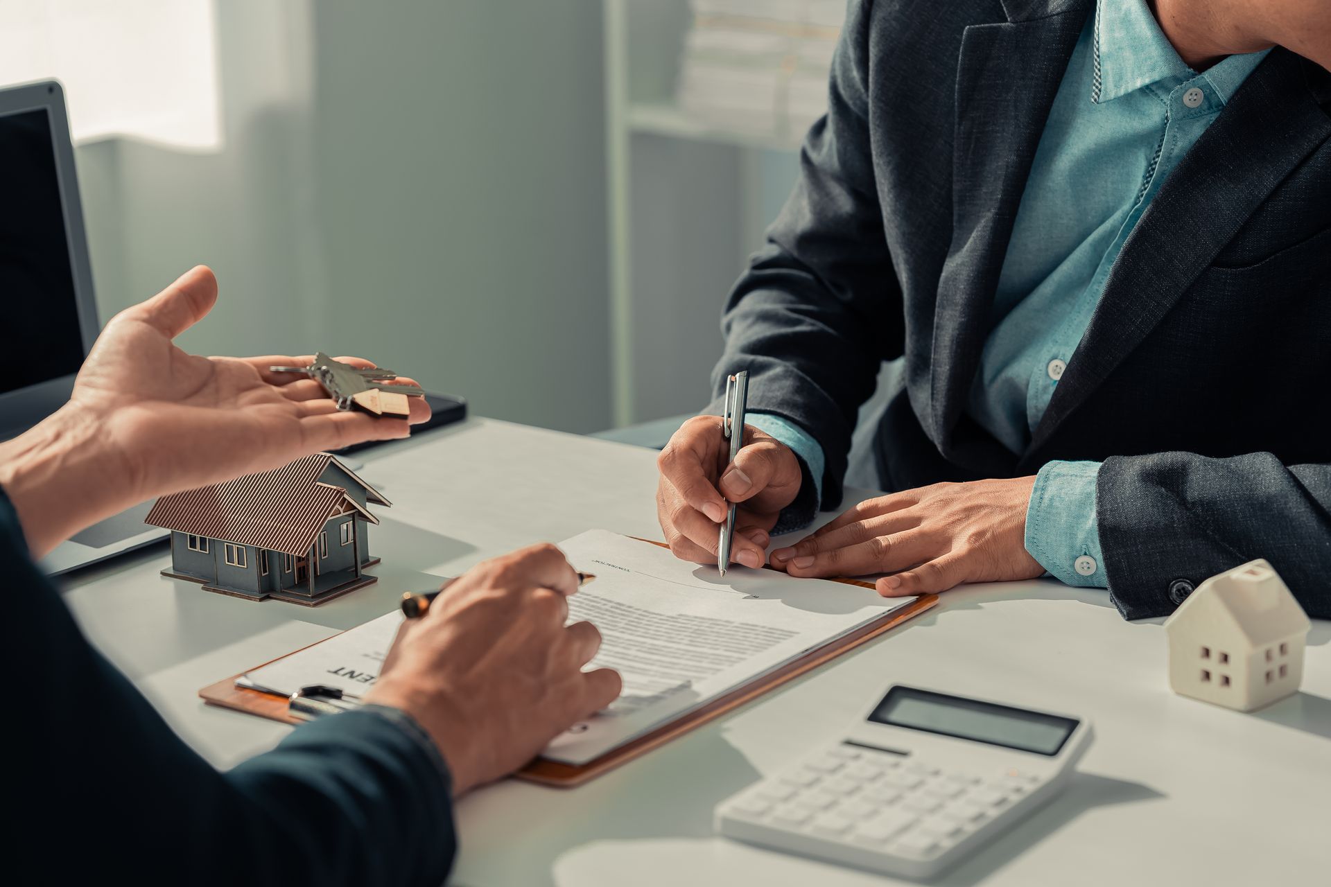 Business meeting with two people signing a document at a desk with a calculator and house model