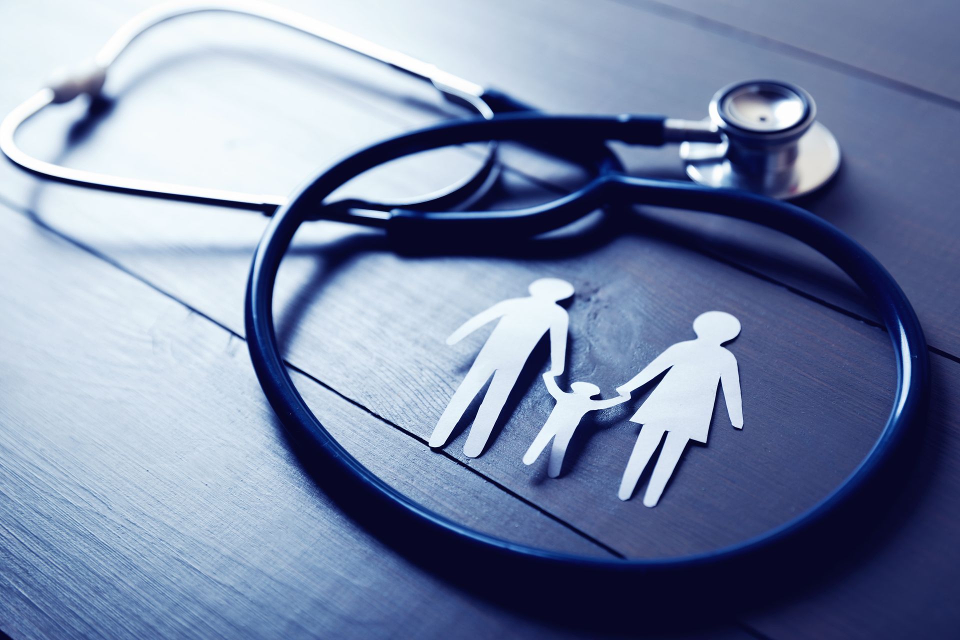 Stethoscope beside paper cutout of family on blue surface