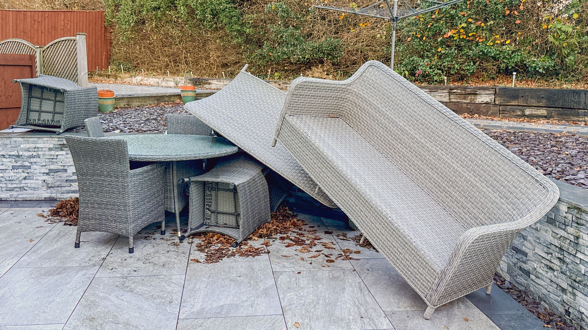 Damaged outdoor patio furniture stacked and toppled on a stone terrace with leaves scattered nearby