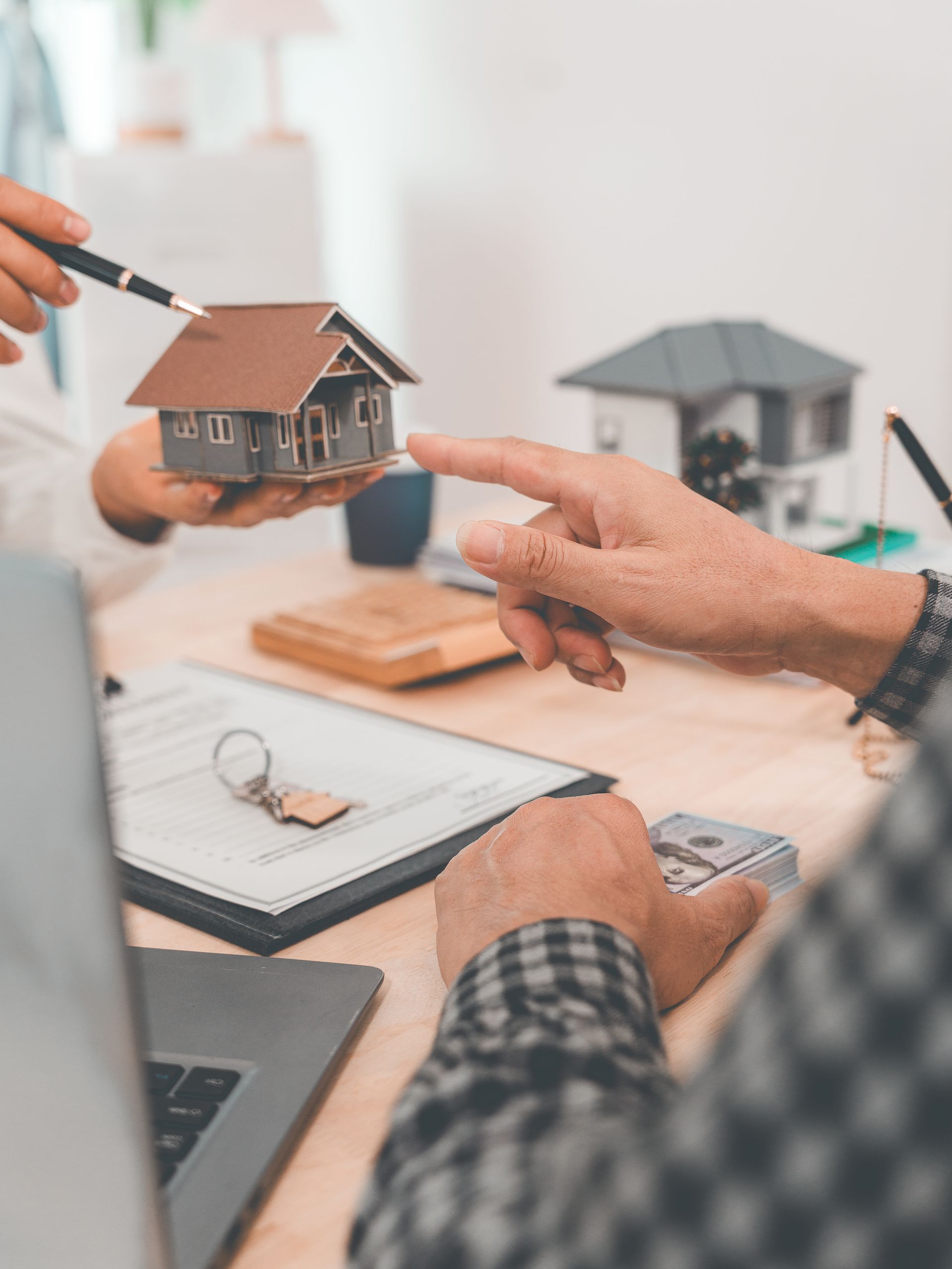 Hands holding a small house model during a real estate consultation at a desk