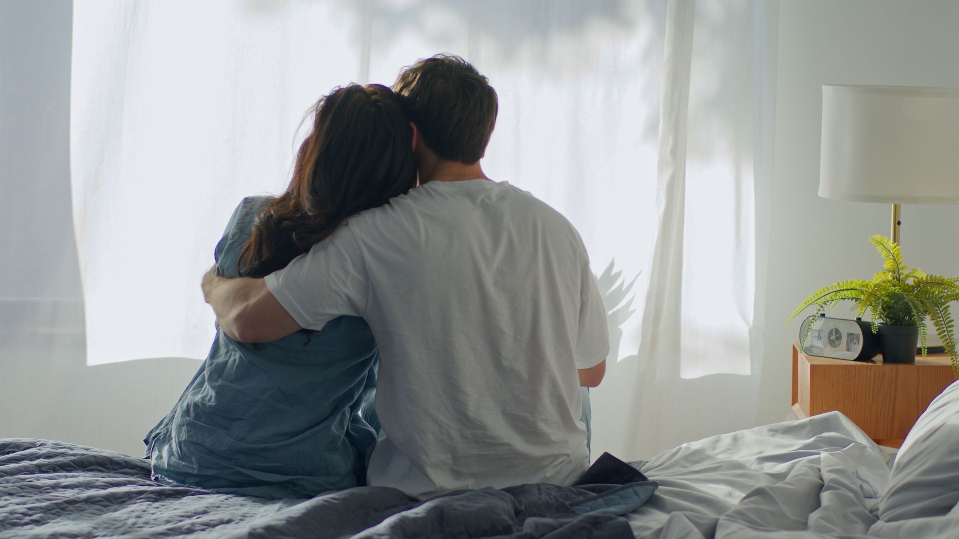 Couple sitting on a bed and embracing in a bright bedroom near a window