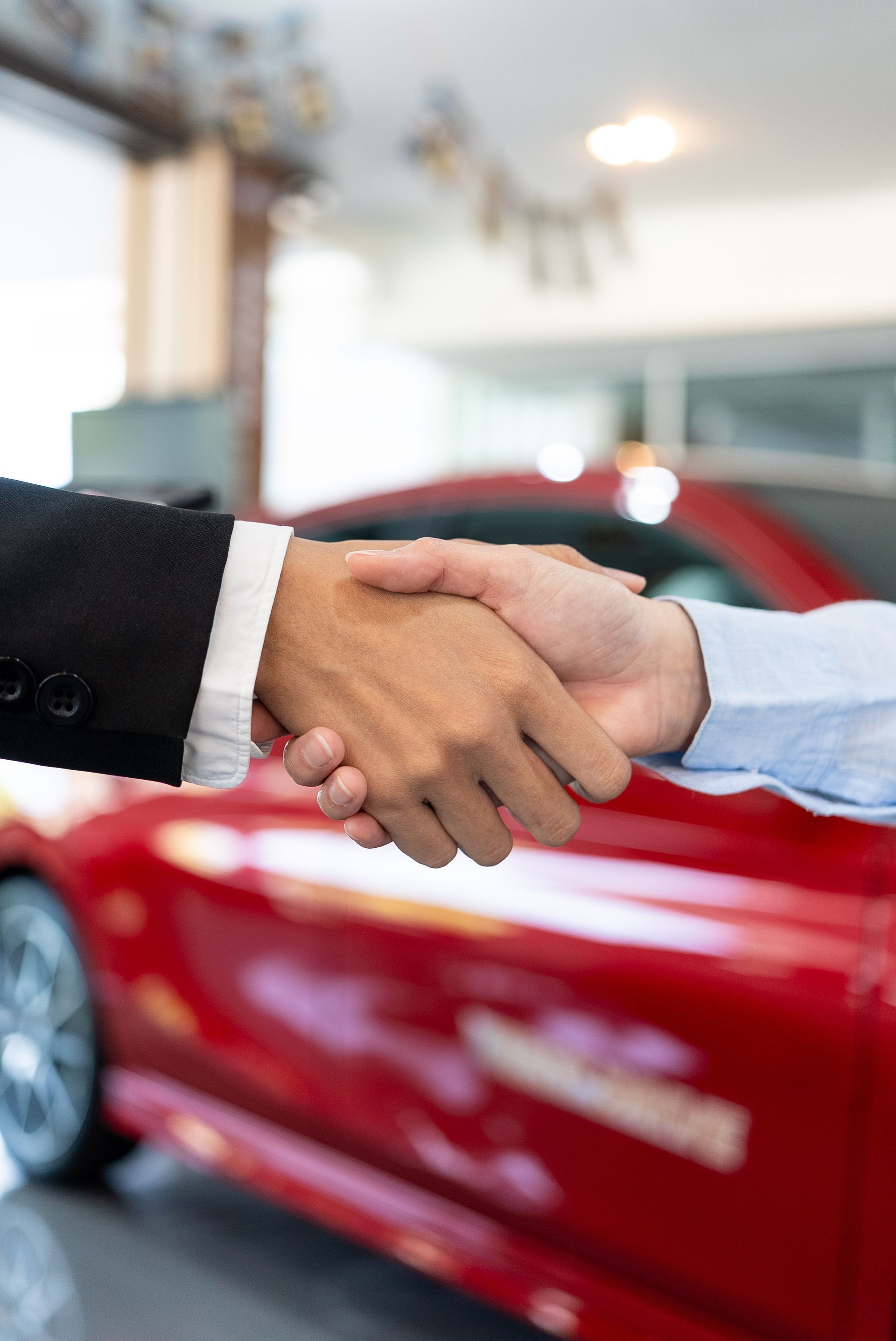 Handshake in front of a red car at a dealership