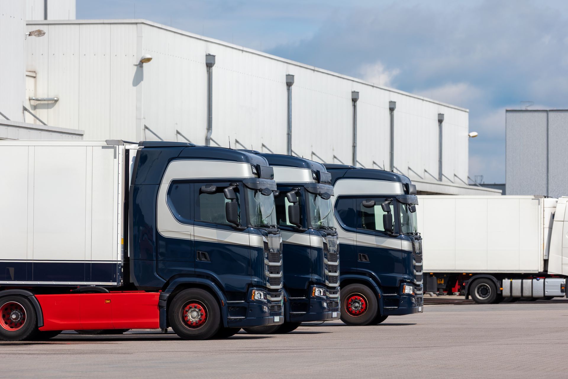 Two blue and red semi trucks parked outside a white warehouse.
