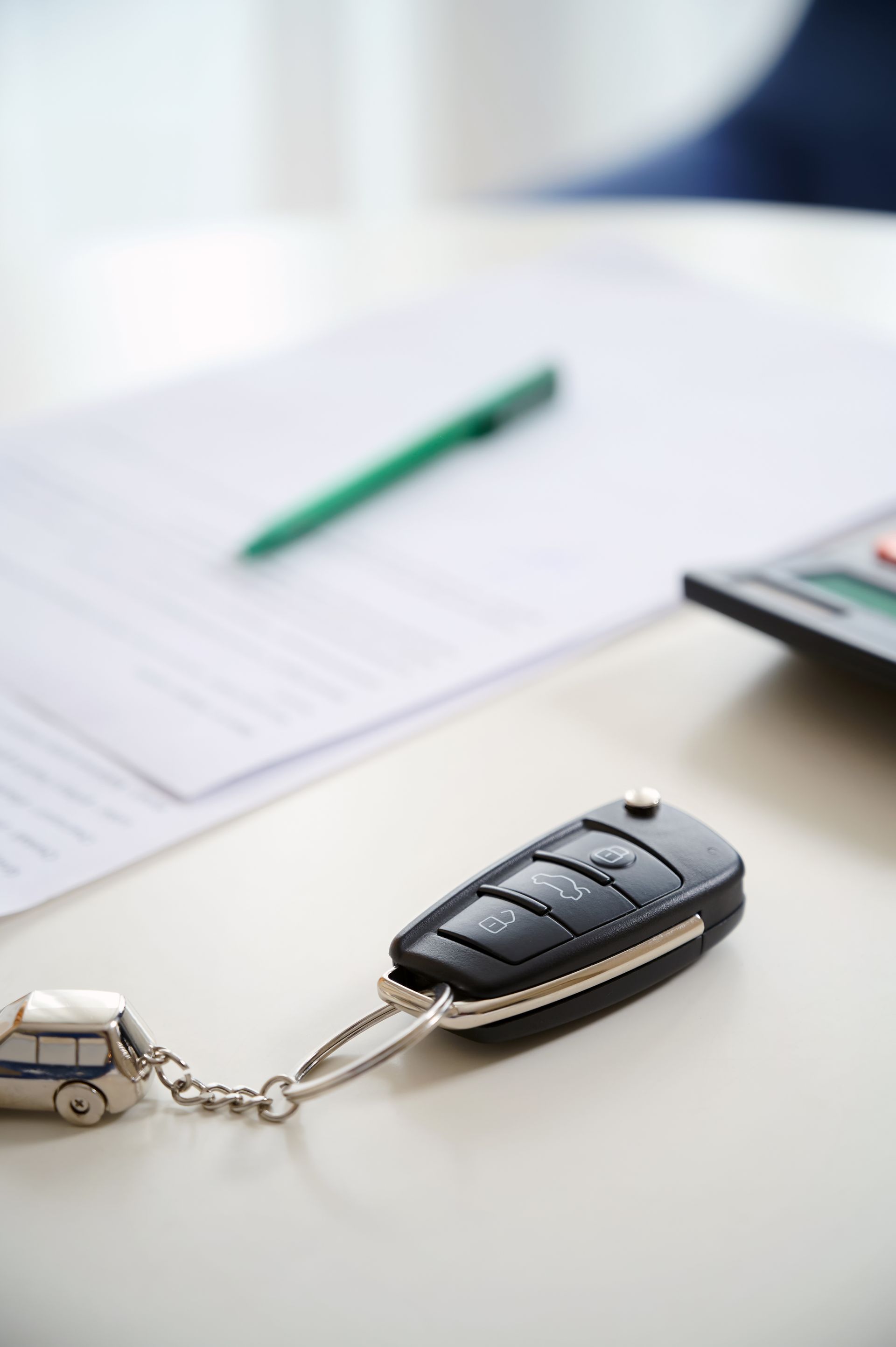 Car key fob on a chain beside a small toy car on a desk with papers and a green pen