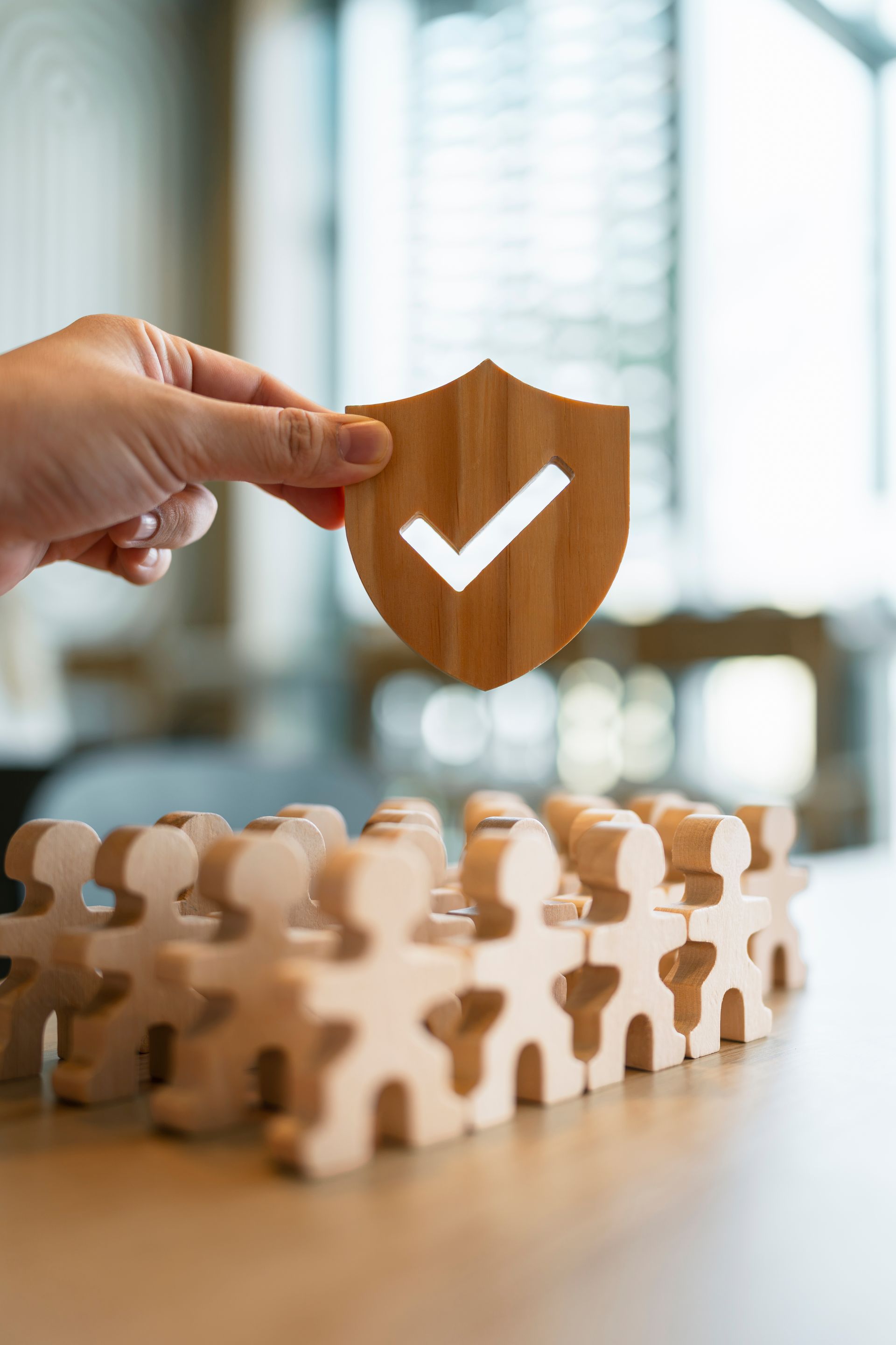 Hand placing a shield with checkmark over a row of wooden puzzle figures
