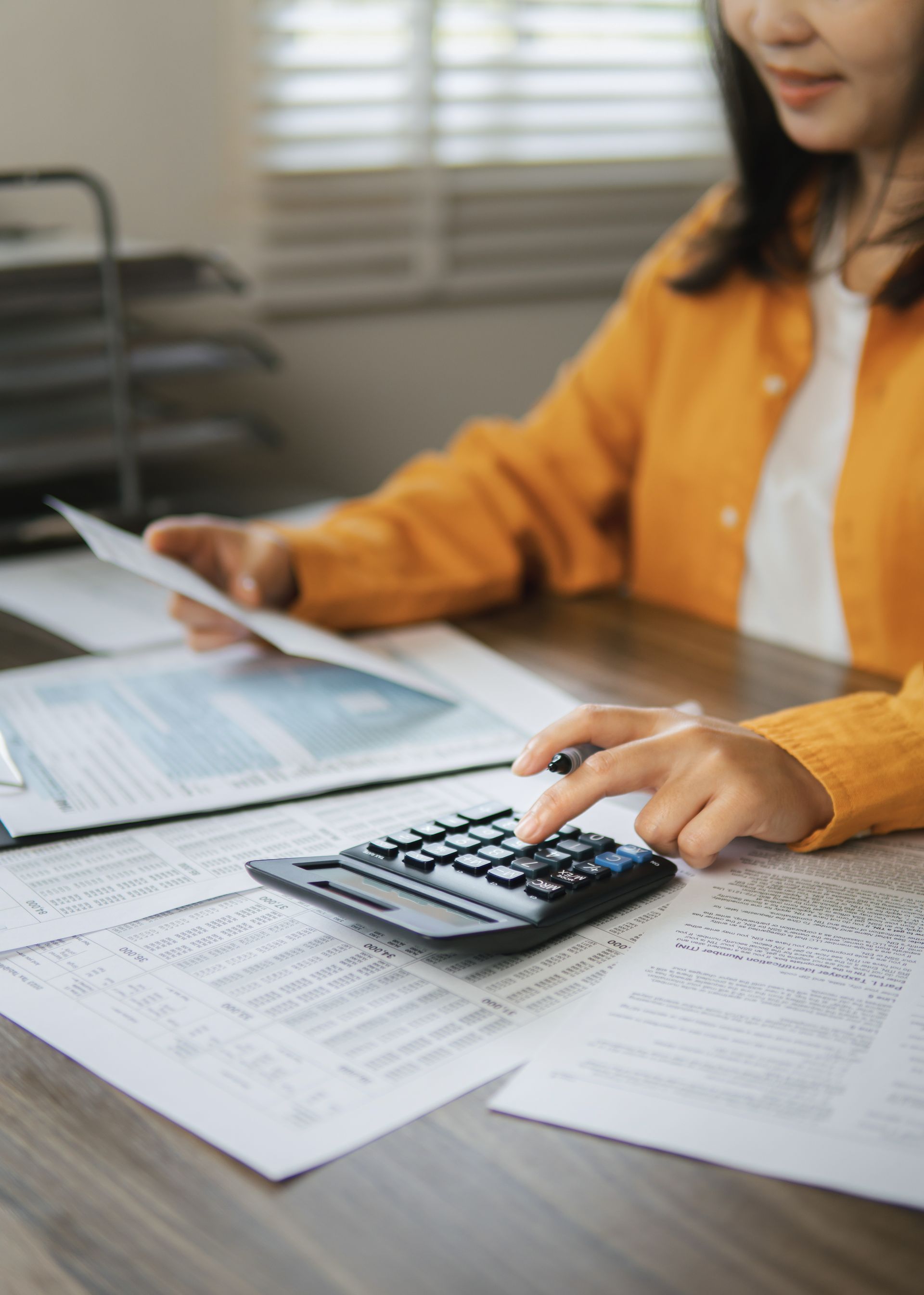 Person using a calculator on paperwork at a desk, with a laptop nearby