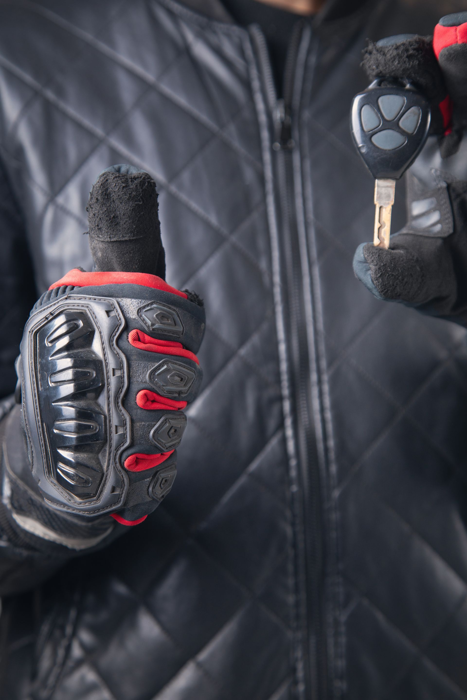 Black and red padded gloves holding a key in front of a quilted black jacket background