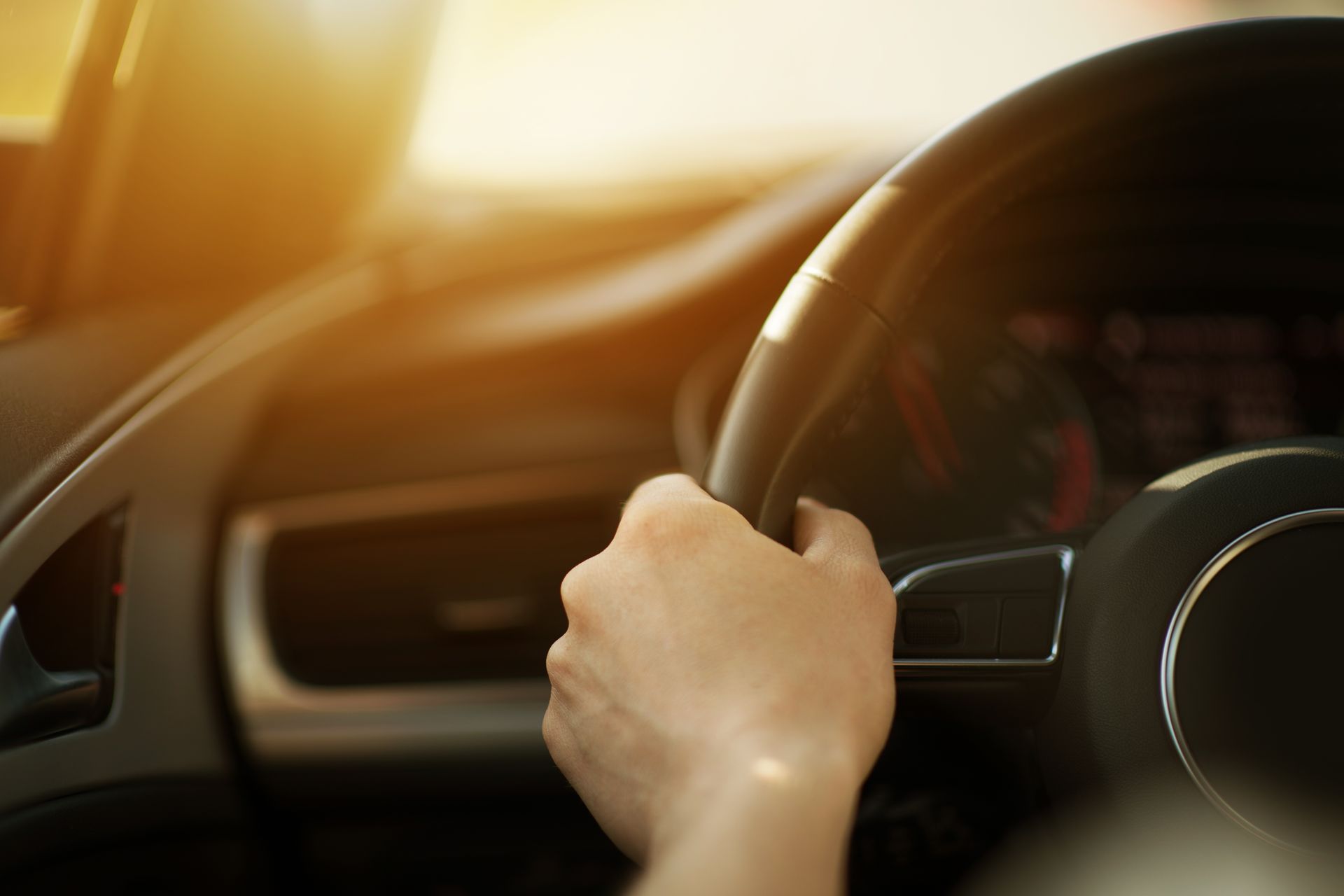 Hand on steering wheel inside a car, with warm sunlight streaming through the windshield.