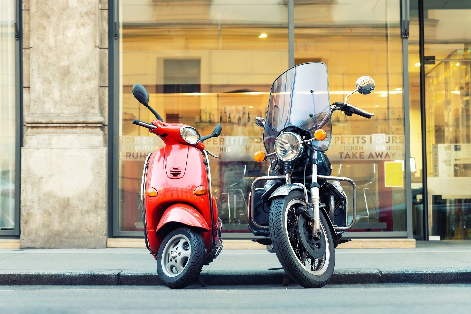 Red scooter and black motorcycle parked outside a glass storefront.