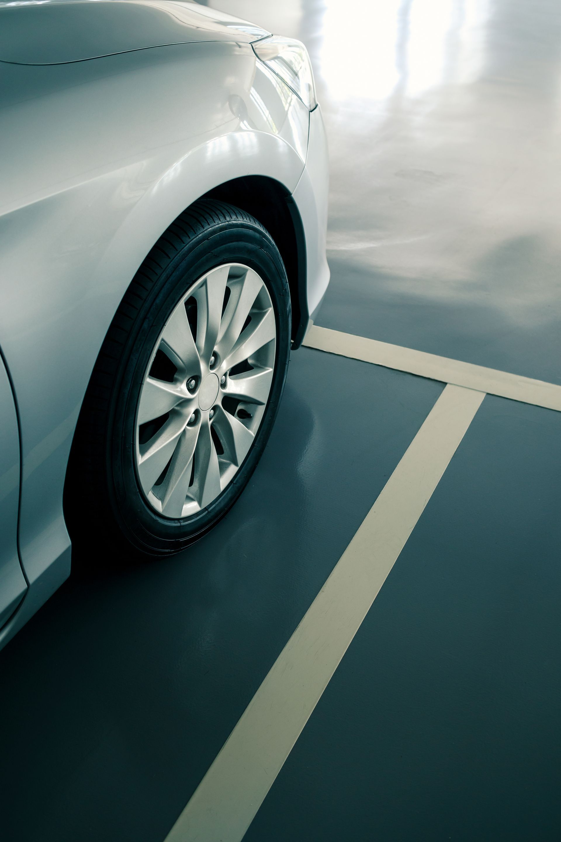 Close-up of a silver car’s front wheel parked in a marked indoor space