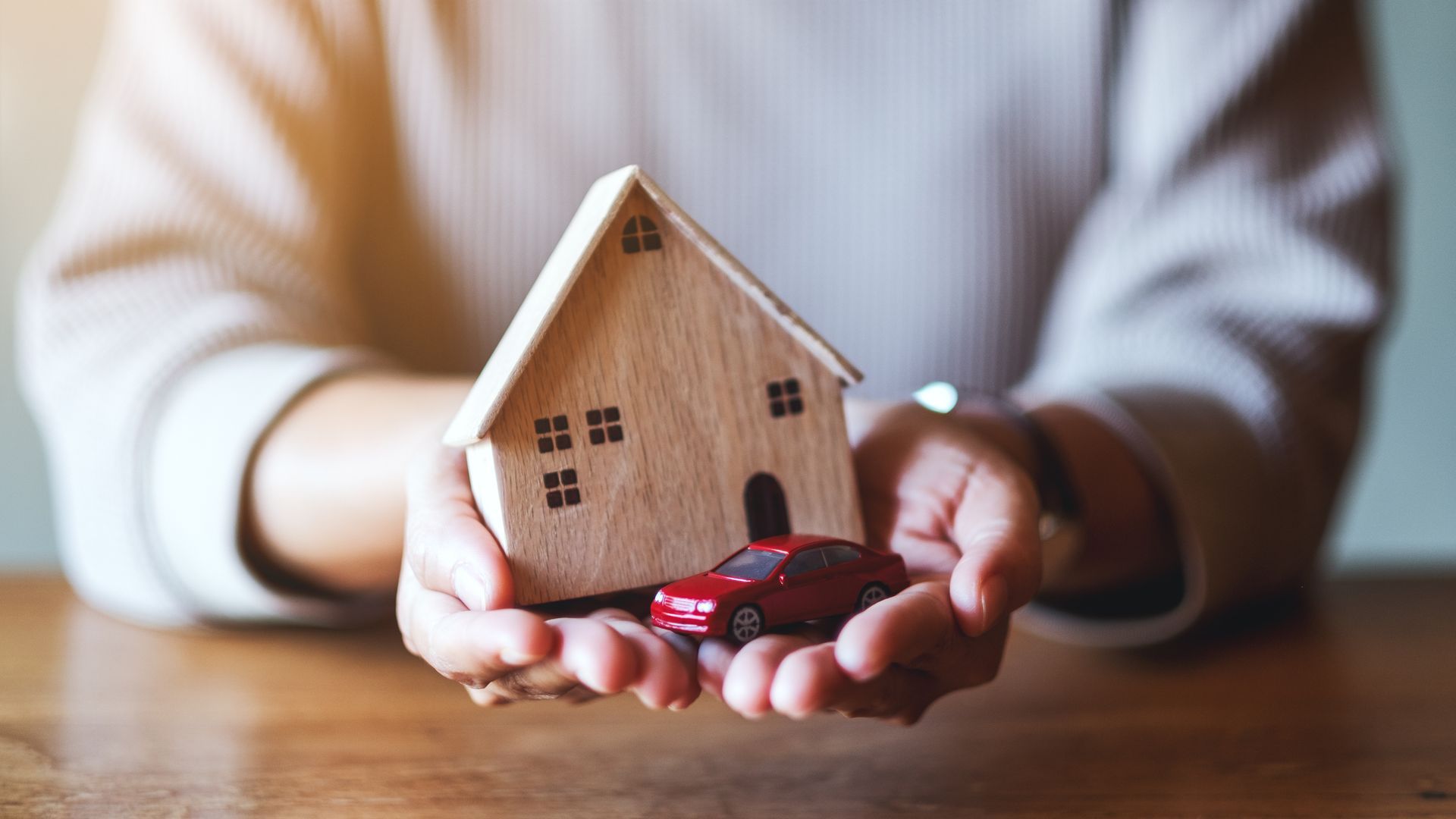 Hands holding a small wooden house with red toy keys on a table