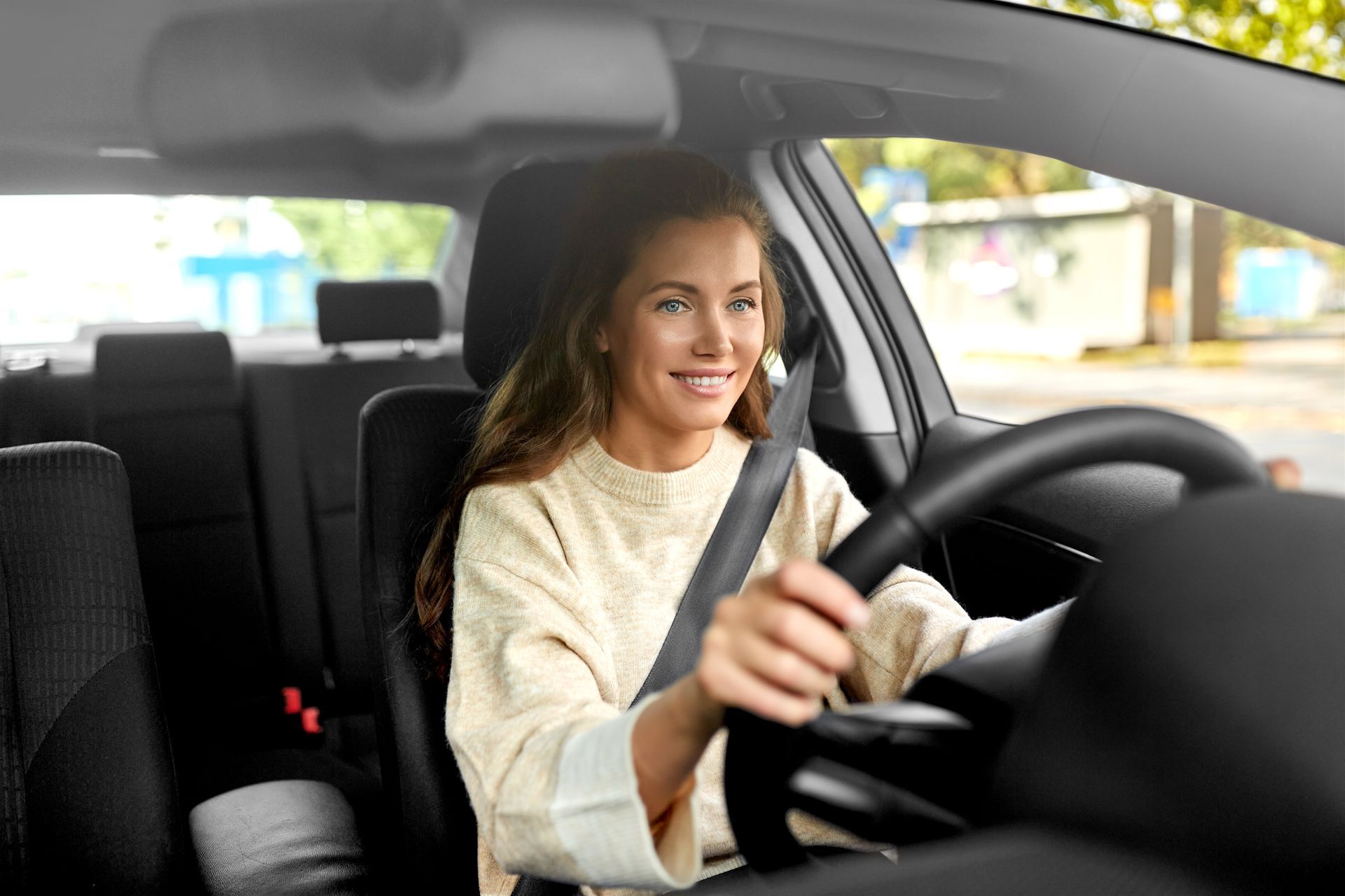 Woman driving a car, smiling with hands on the steering wheel.
