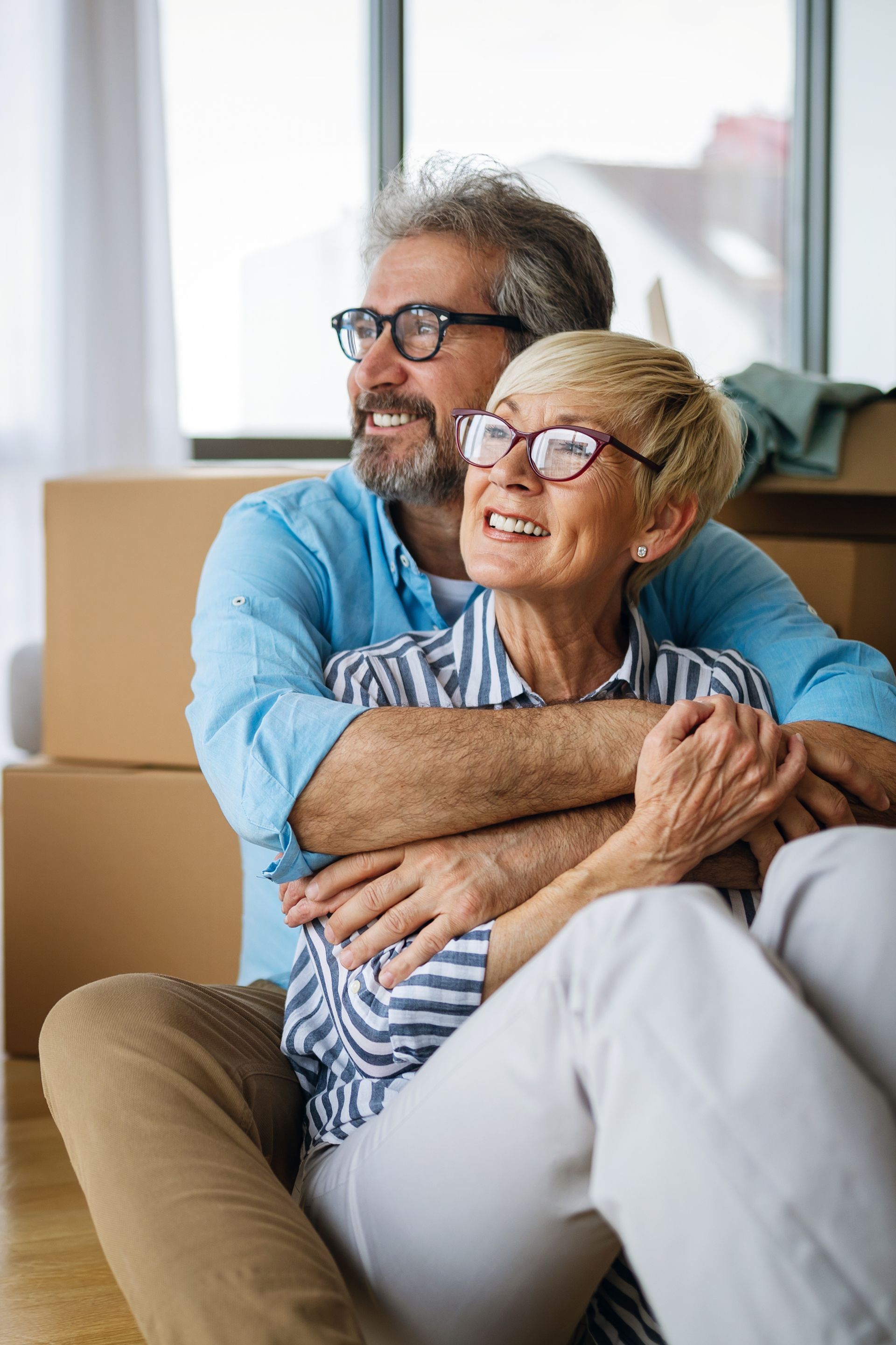 Smiling couple embracing on a couch in a bright living room near moving boxes