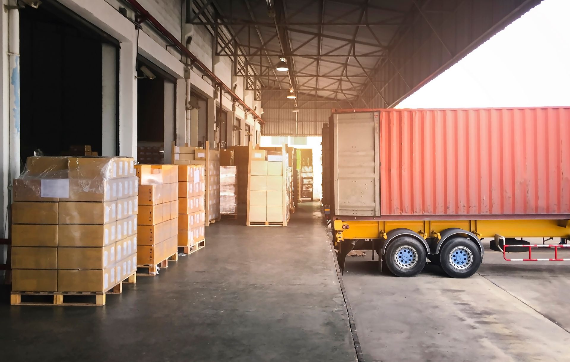 Warehouse loading dock with stacked pallets and a red shipping container on a trailer