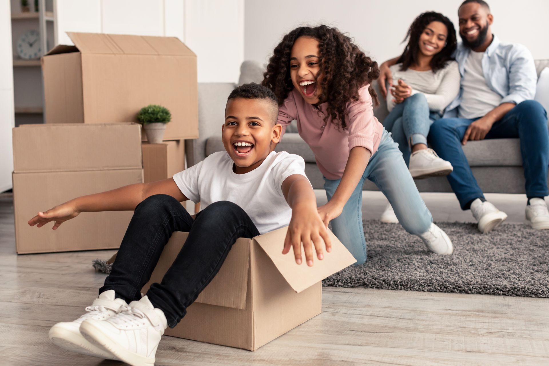 Family playing and smiling during a move, with cardboard boxes in a bright living room.