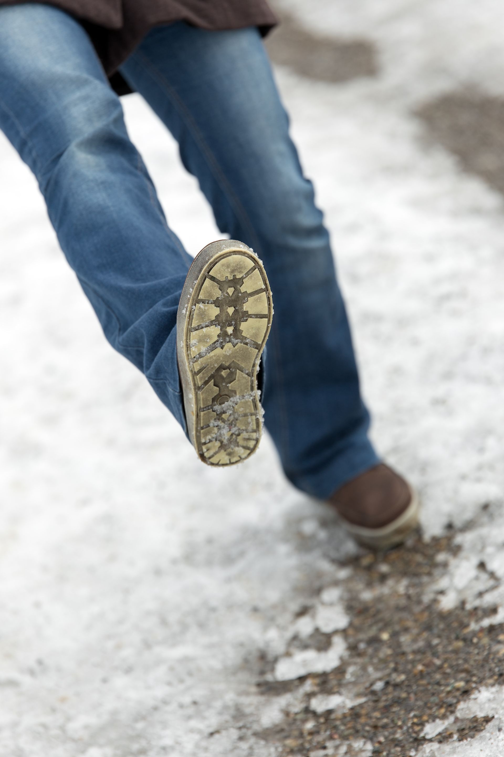 Close-up of legs in jeans stepping on snowy, slushy ground, with one shoe sole facing the camera