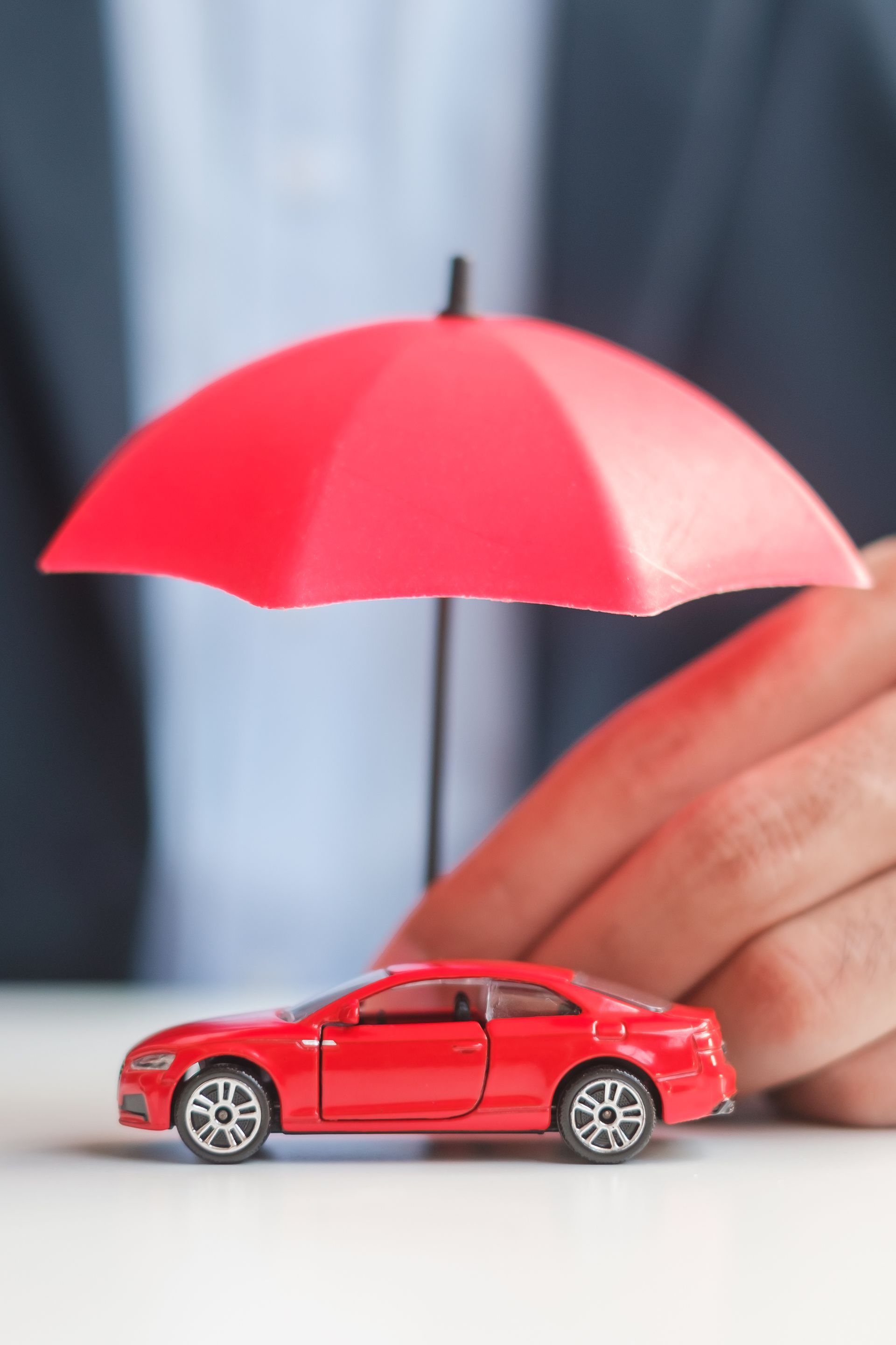 Red toy car sheltered by a red umbrella beside a hand