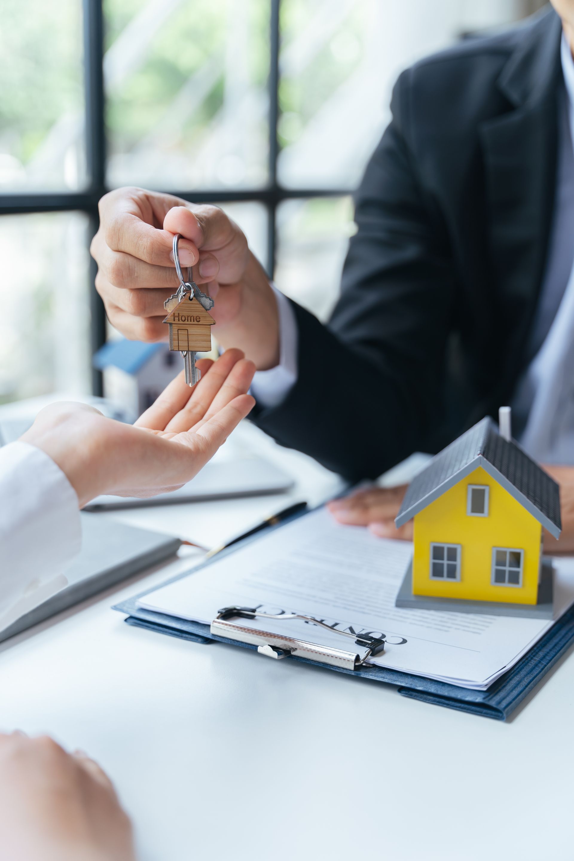 Handing over house keys during a real estate meeting, with a small house model on the desk
