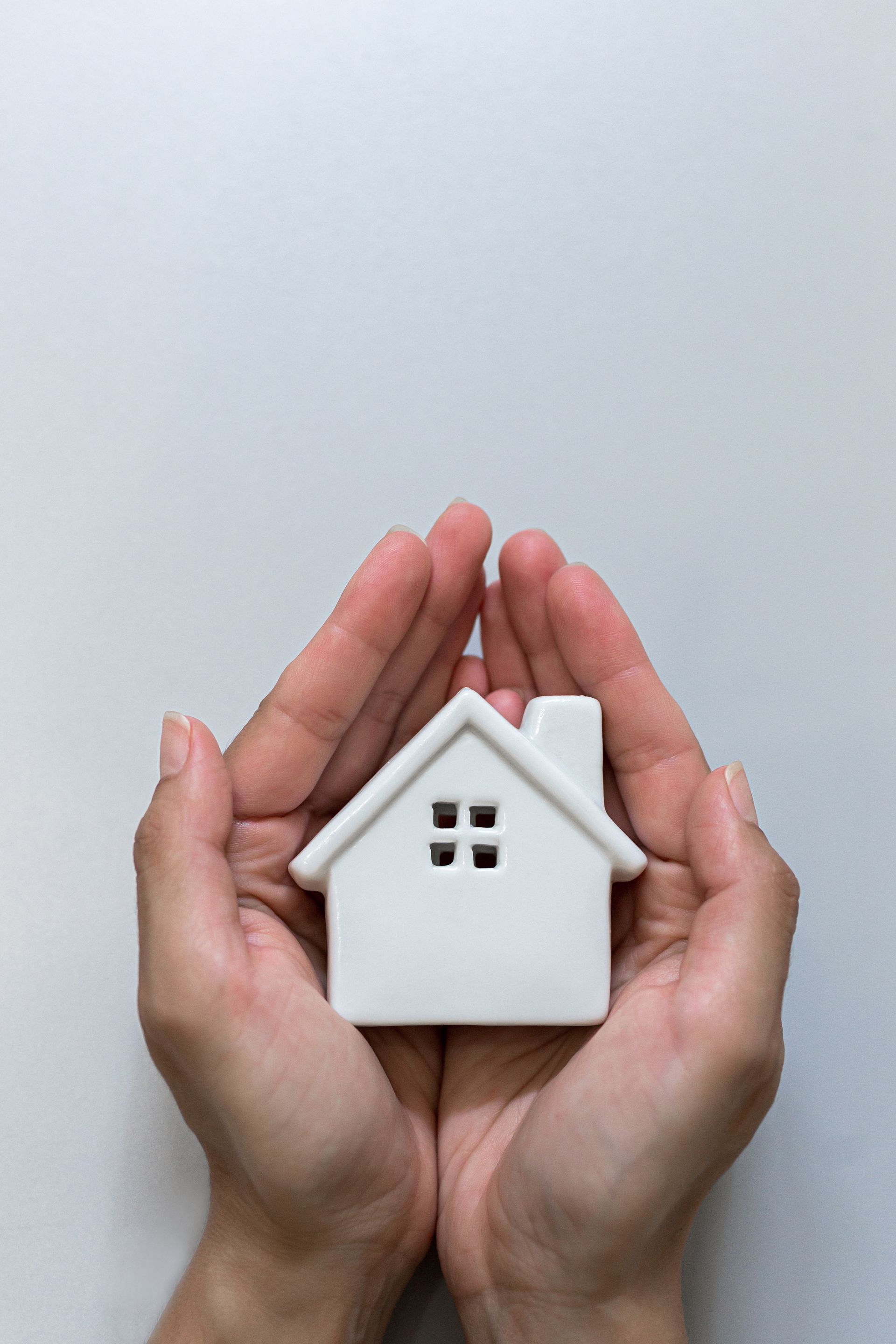 Hands cupping a small white house model against a light gray background