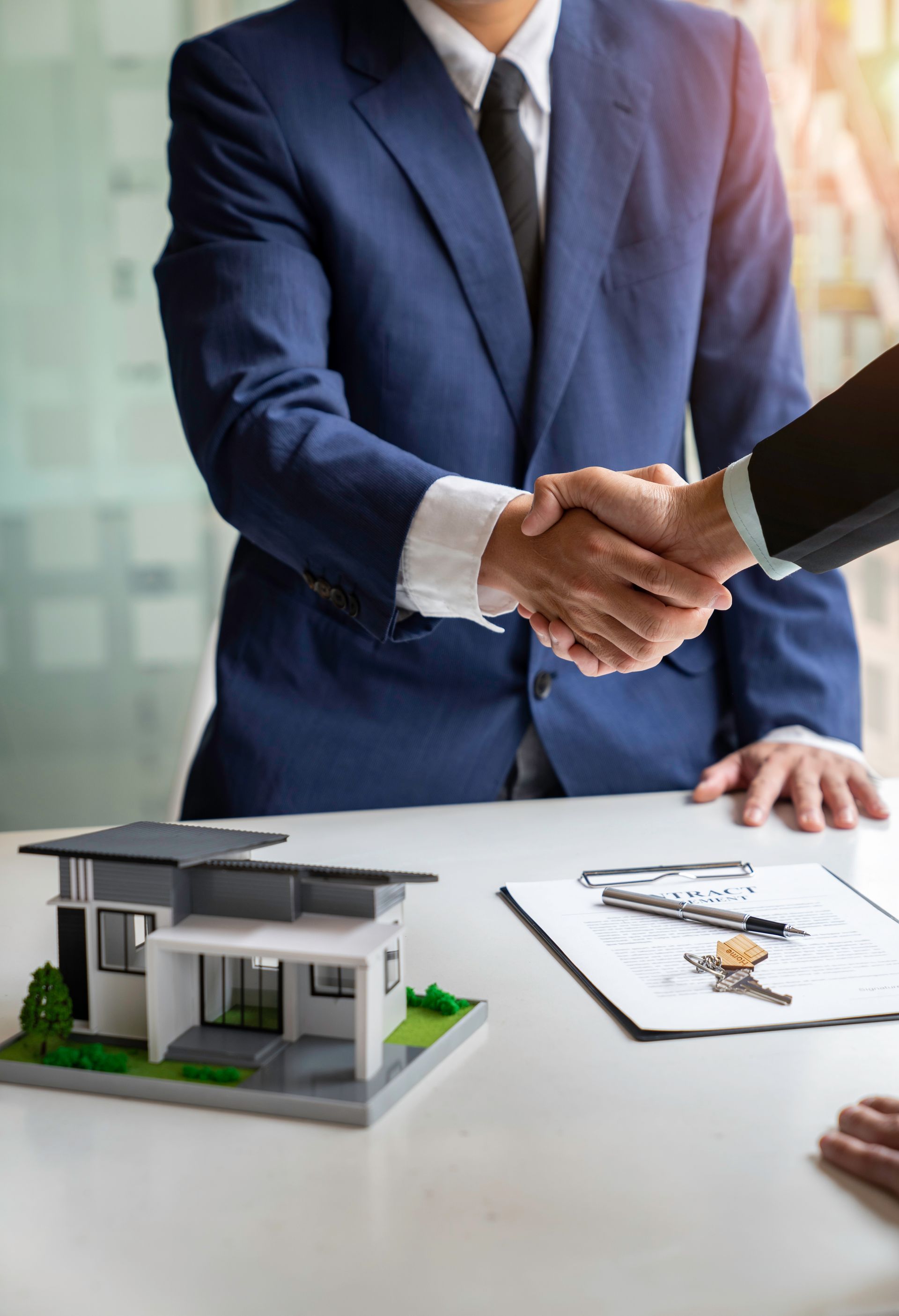 Business handshake over a desk with a house model and signed documents