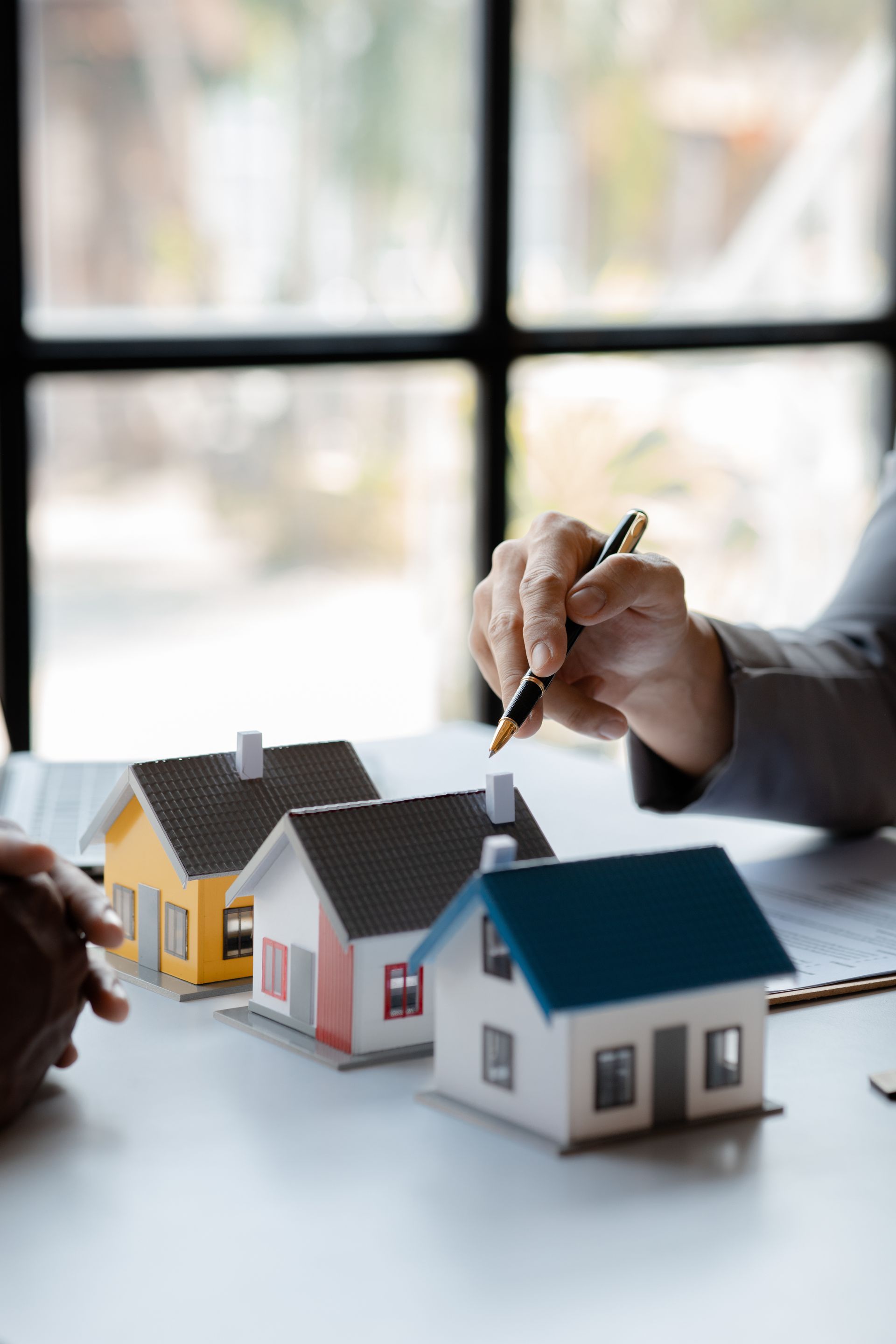 Hands arranging model houses on a desk during a real estate meeting