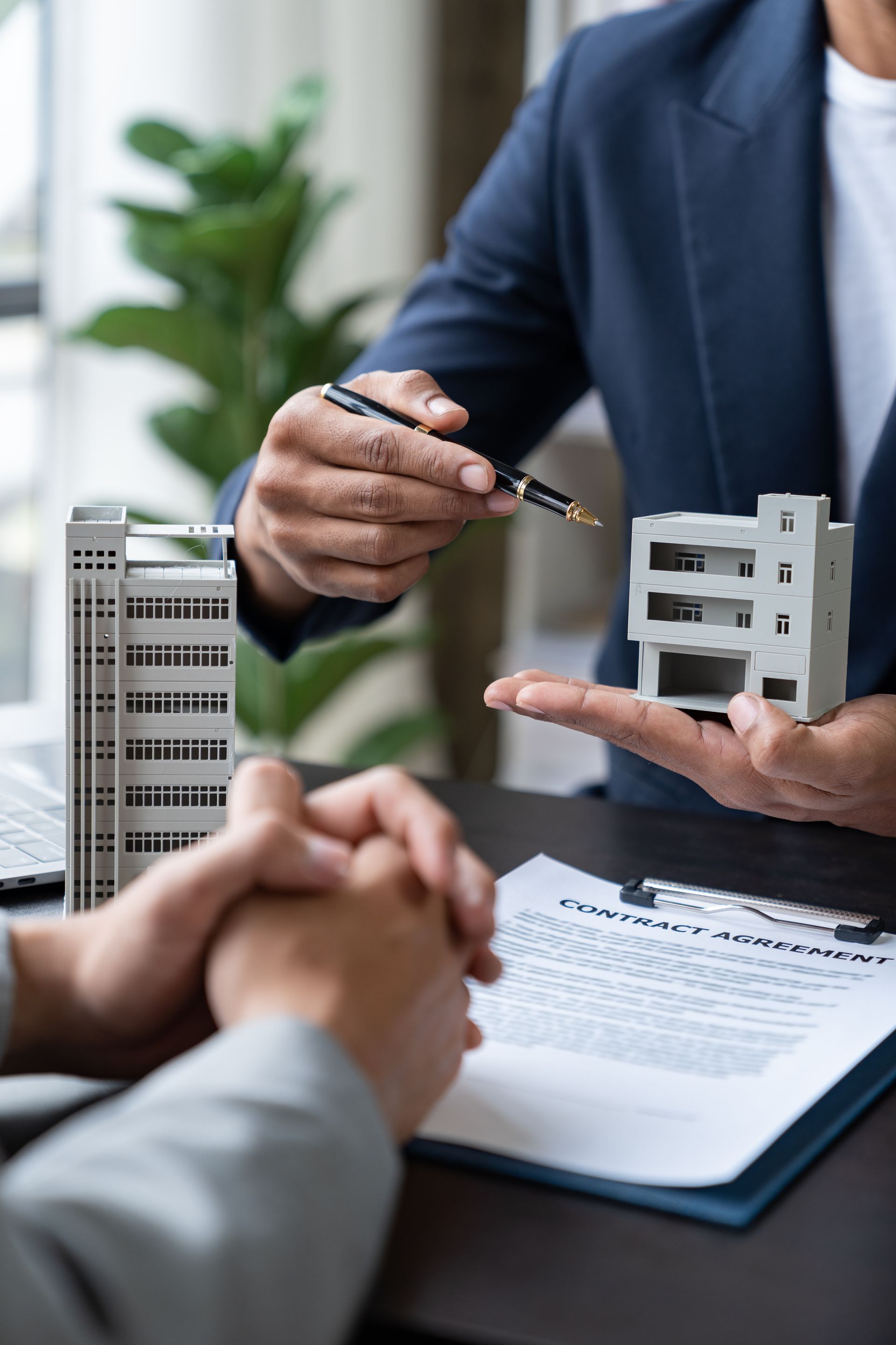 Business meeting with hand presenting a building model over a signed contract on a desk