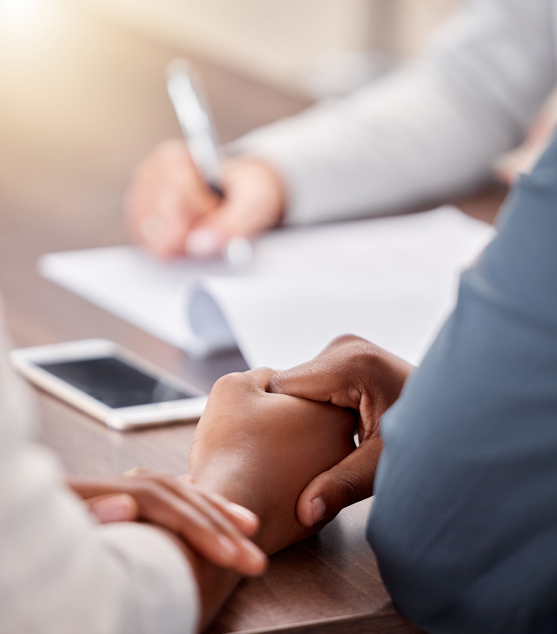 Hands clasped in a meeting with a smartphone and notebook on the table