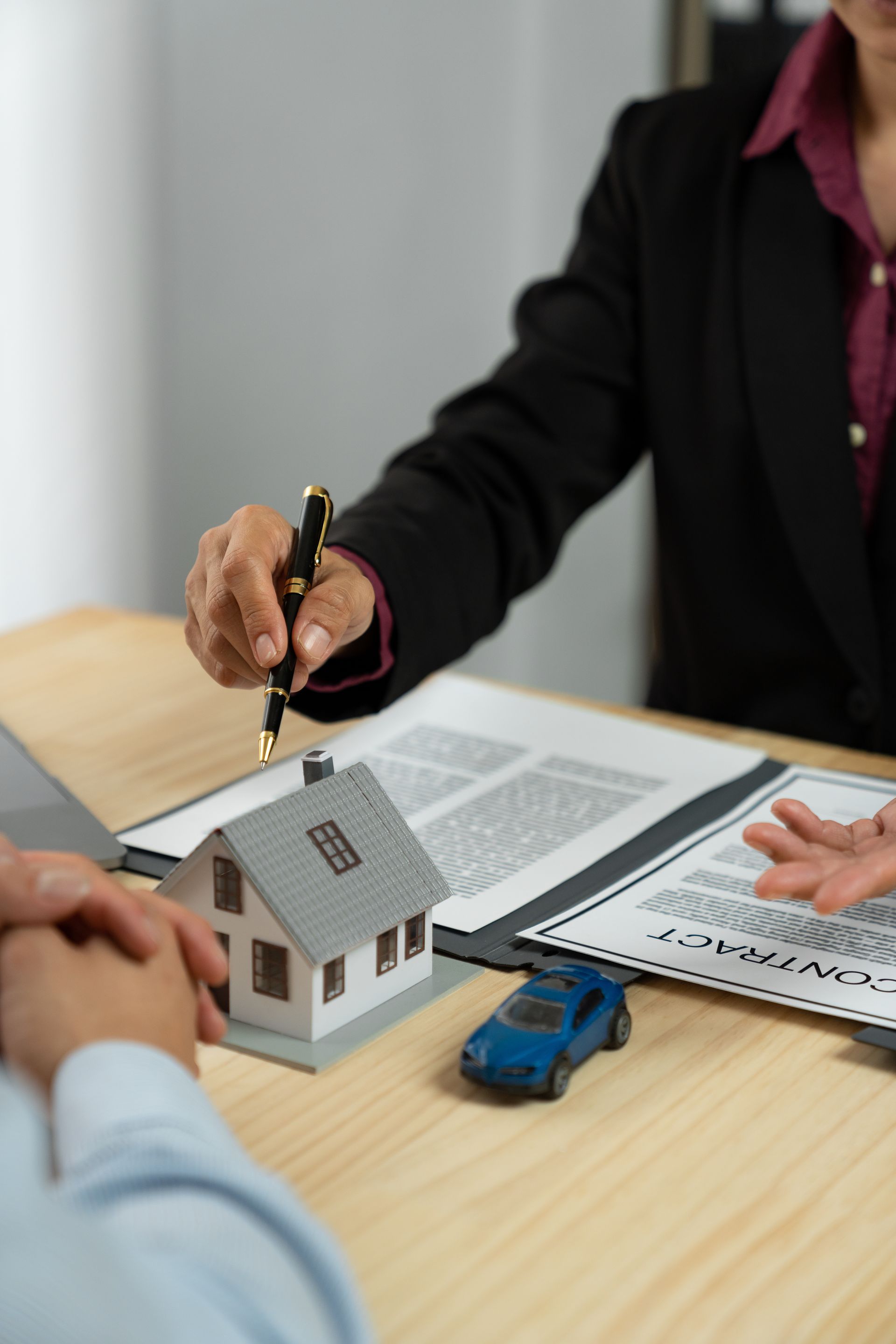 Hands exchanging house keys over a real estate contract beside a small model house and blue toy car.