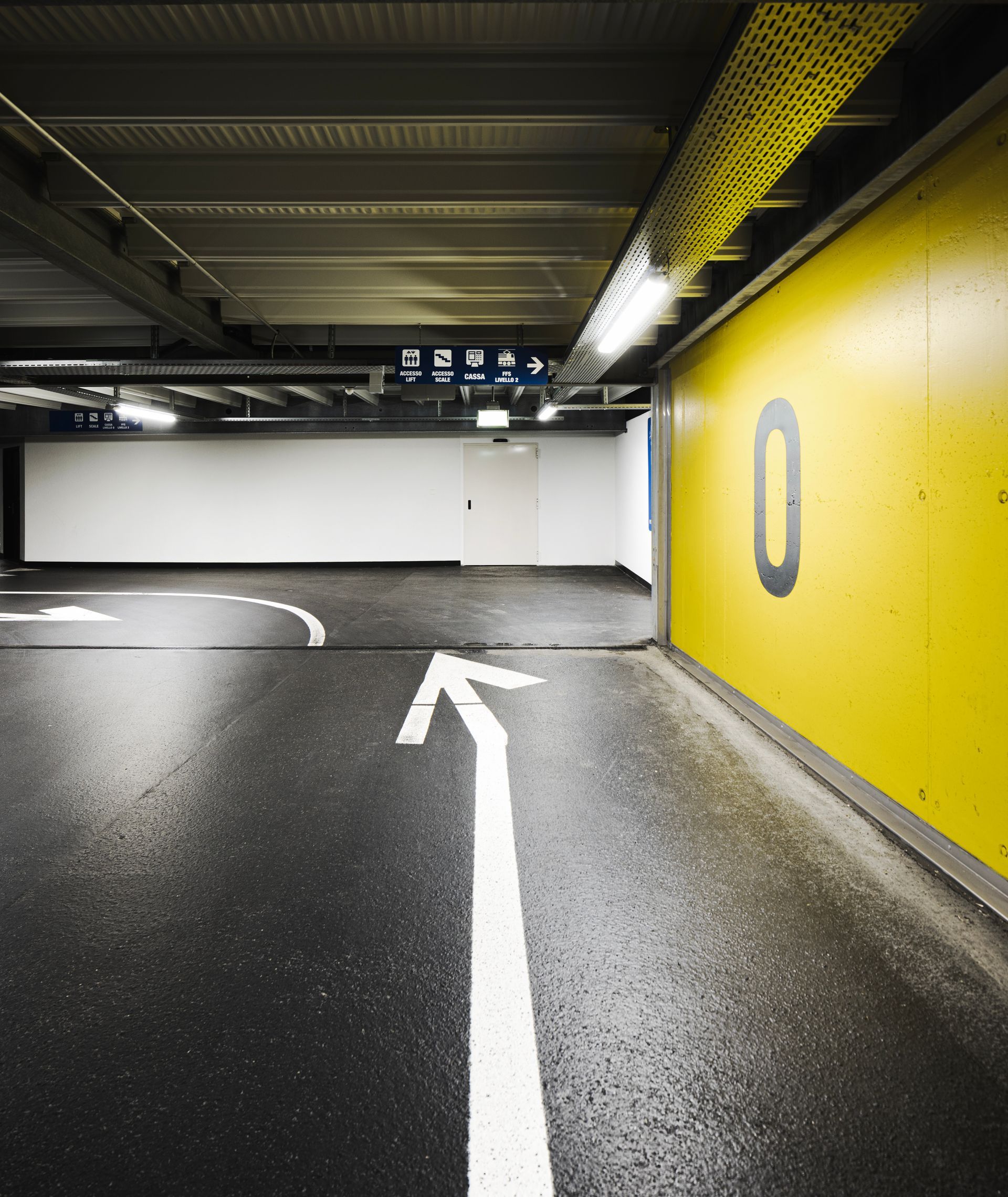 Parking garage lane with white directional arrow and yellow wall marked “0”