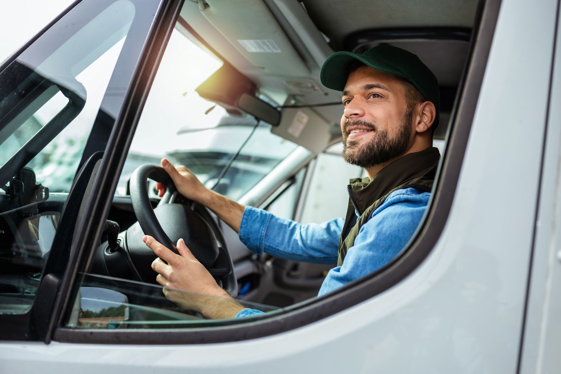 Driver smiling inside a white truck cab, holding the steering wheel and looking ahead.