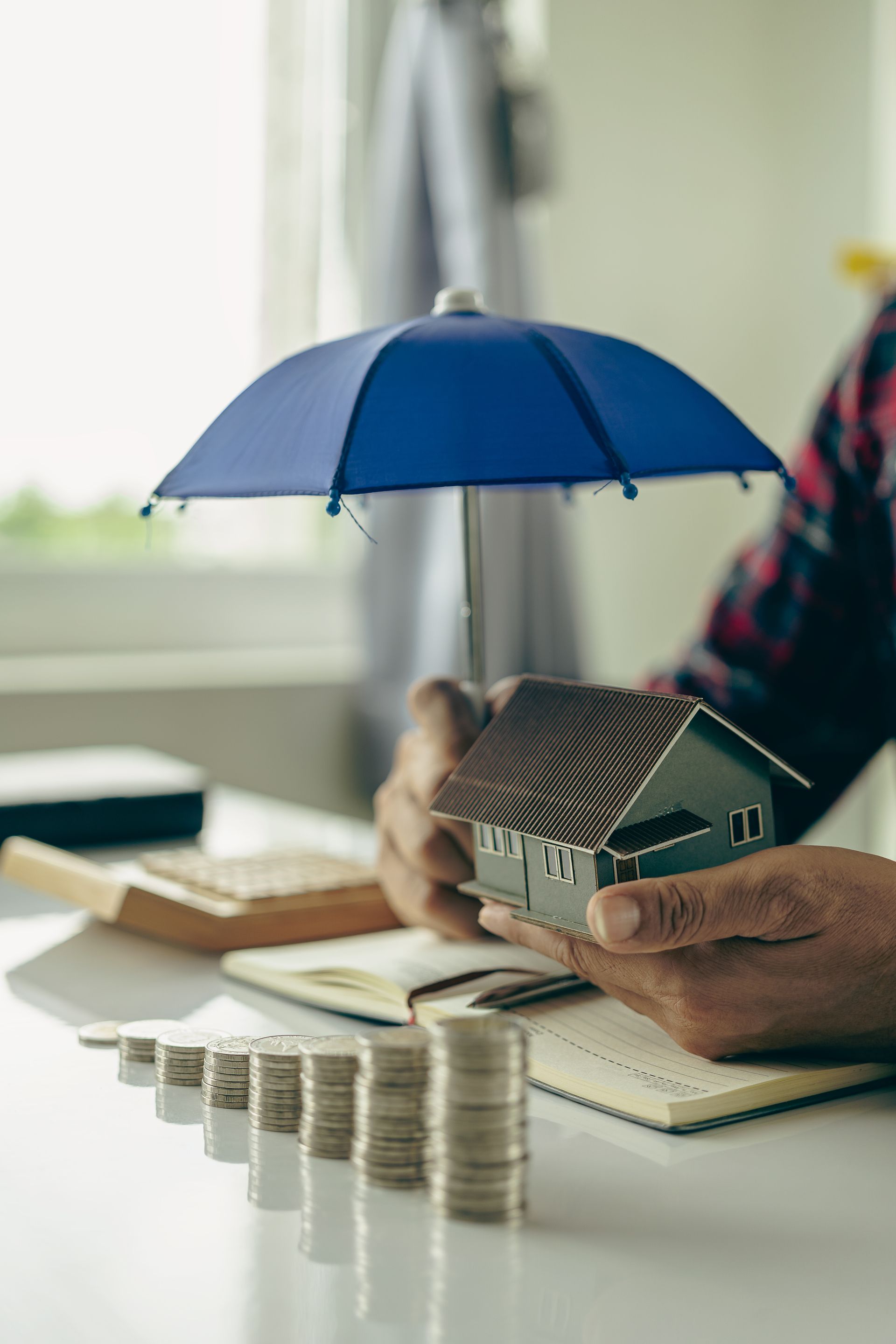 Blue umbrella over house model and stacked coins on a desk