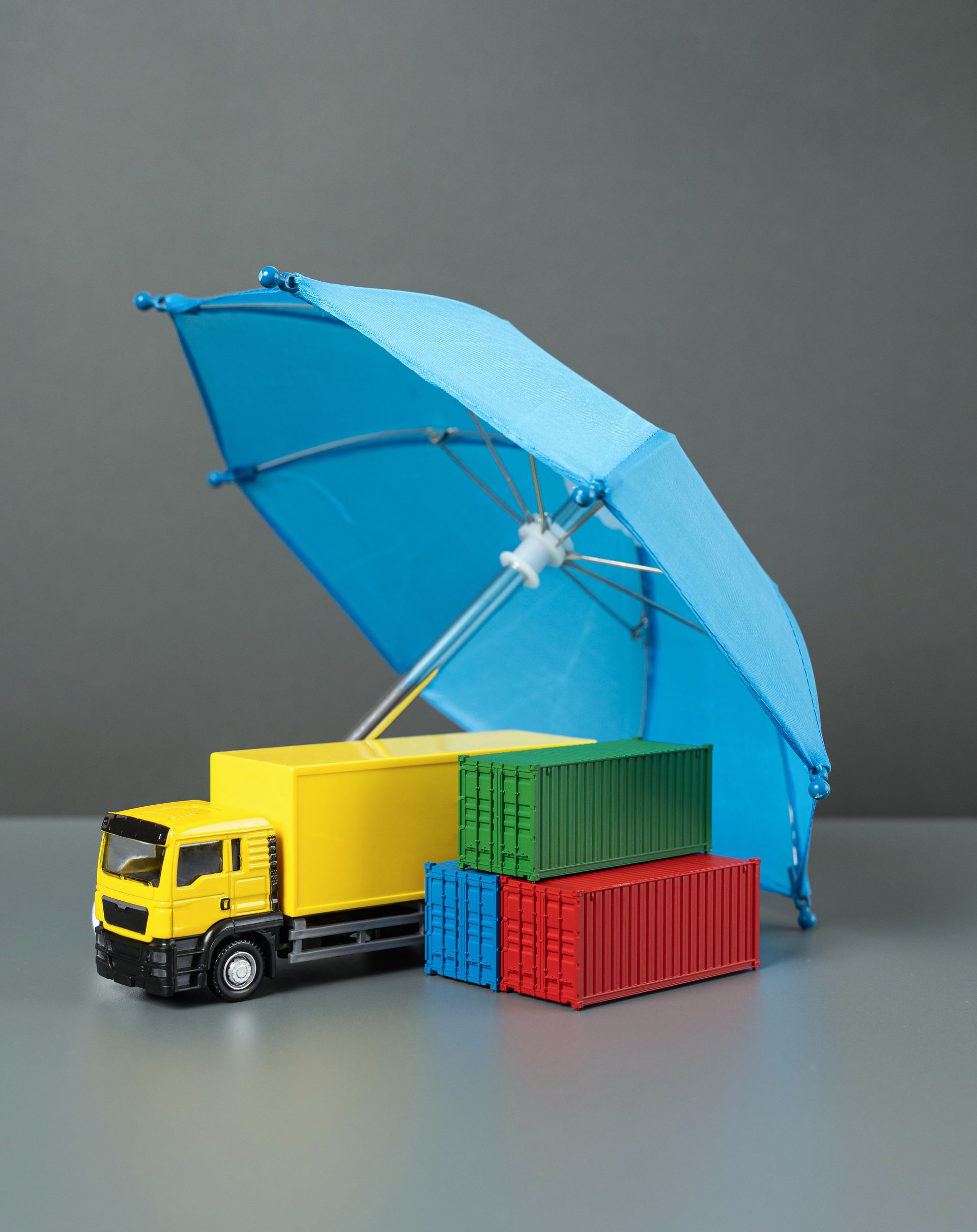 Toy delivery truck with blue umbrella canopy and stacked shipping containers on a gray background