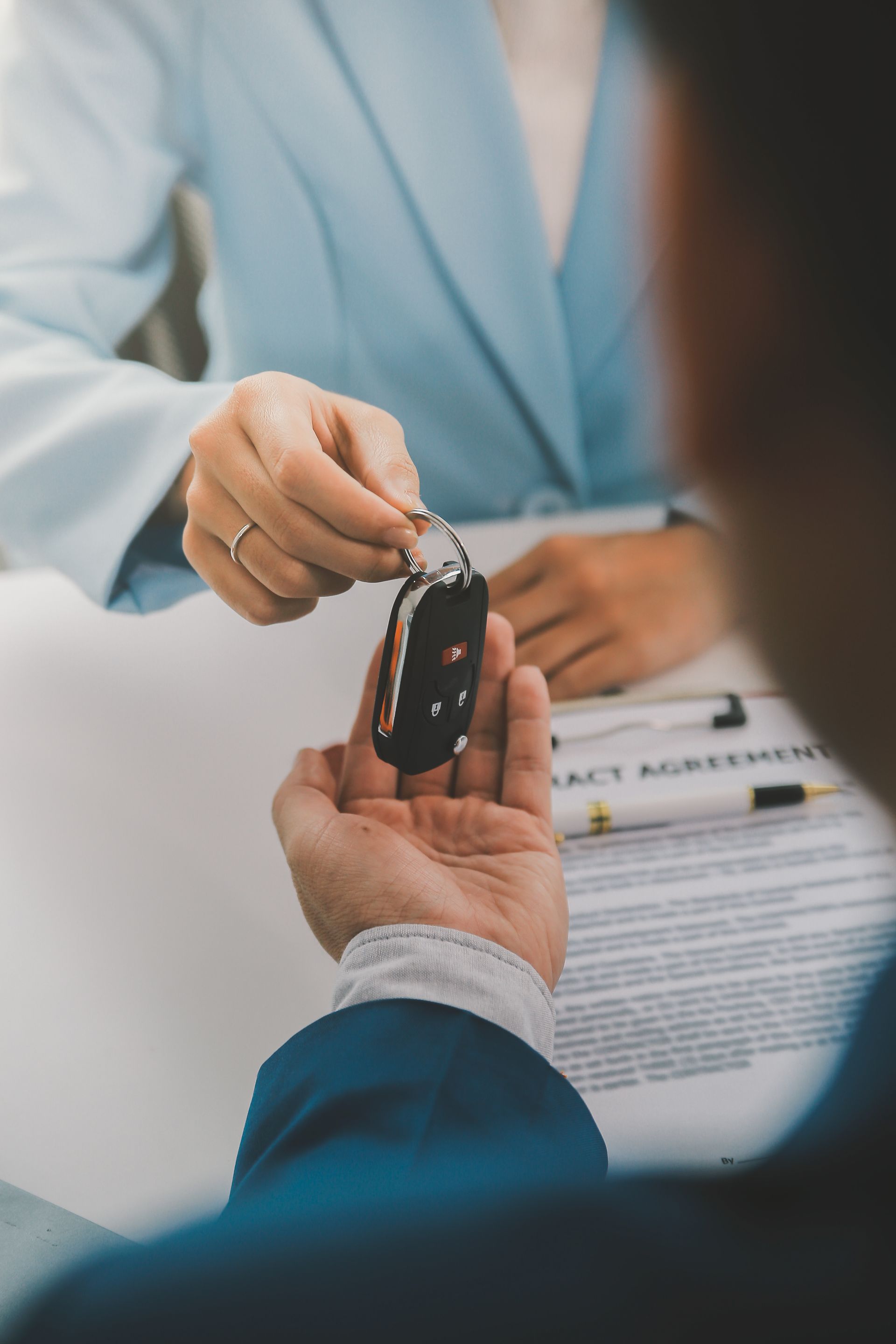 Person handing car keys to another person over paperwork at a desk