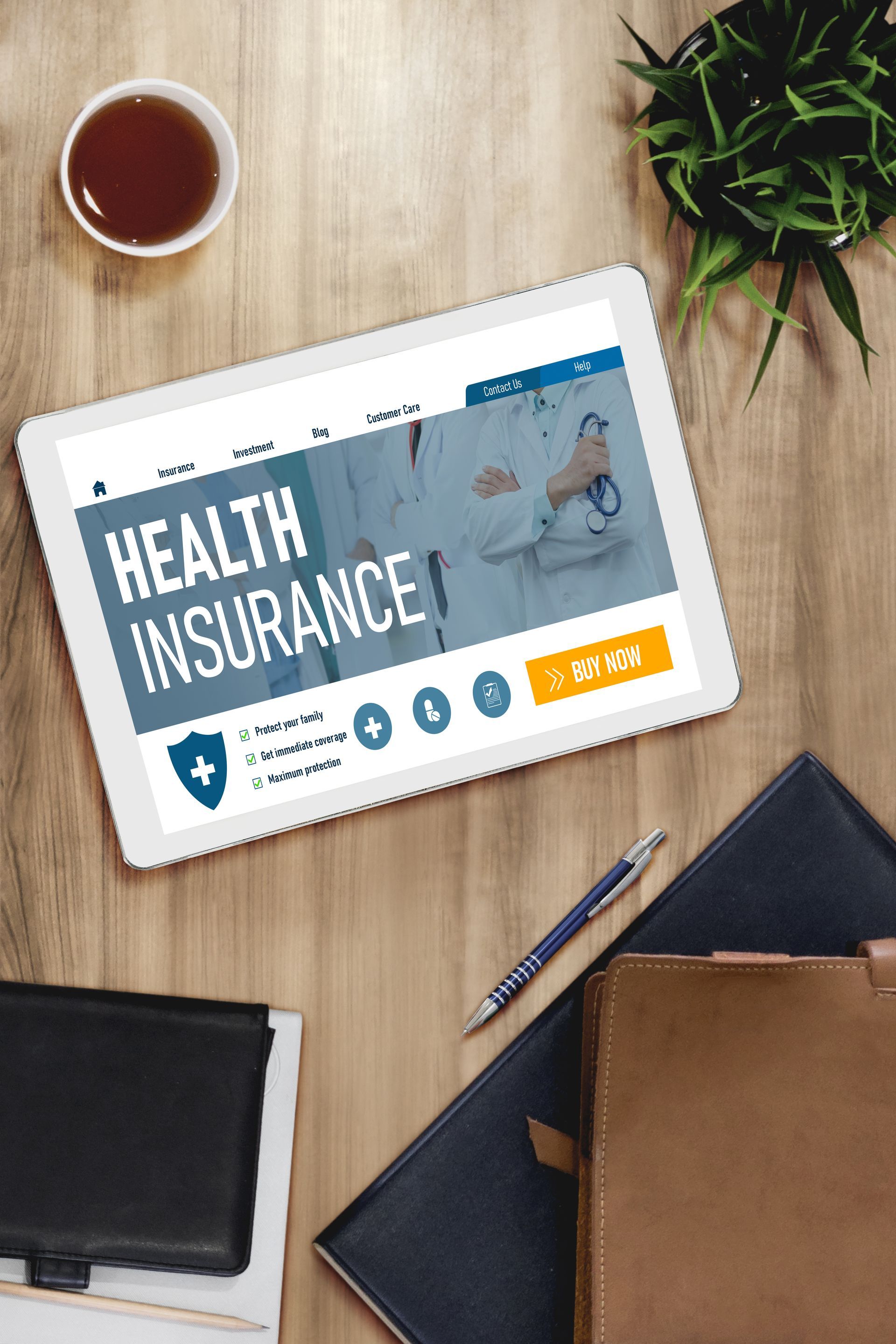 Tablet showing health insurance page on a desk with coffee, plant, notebooks, and pen
