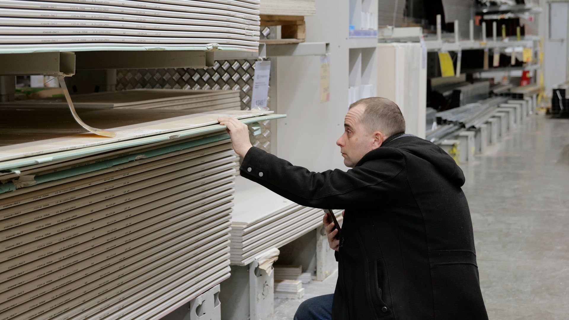 Contractor inspecting stacked drywall panels at a building supply store.