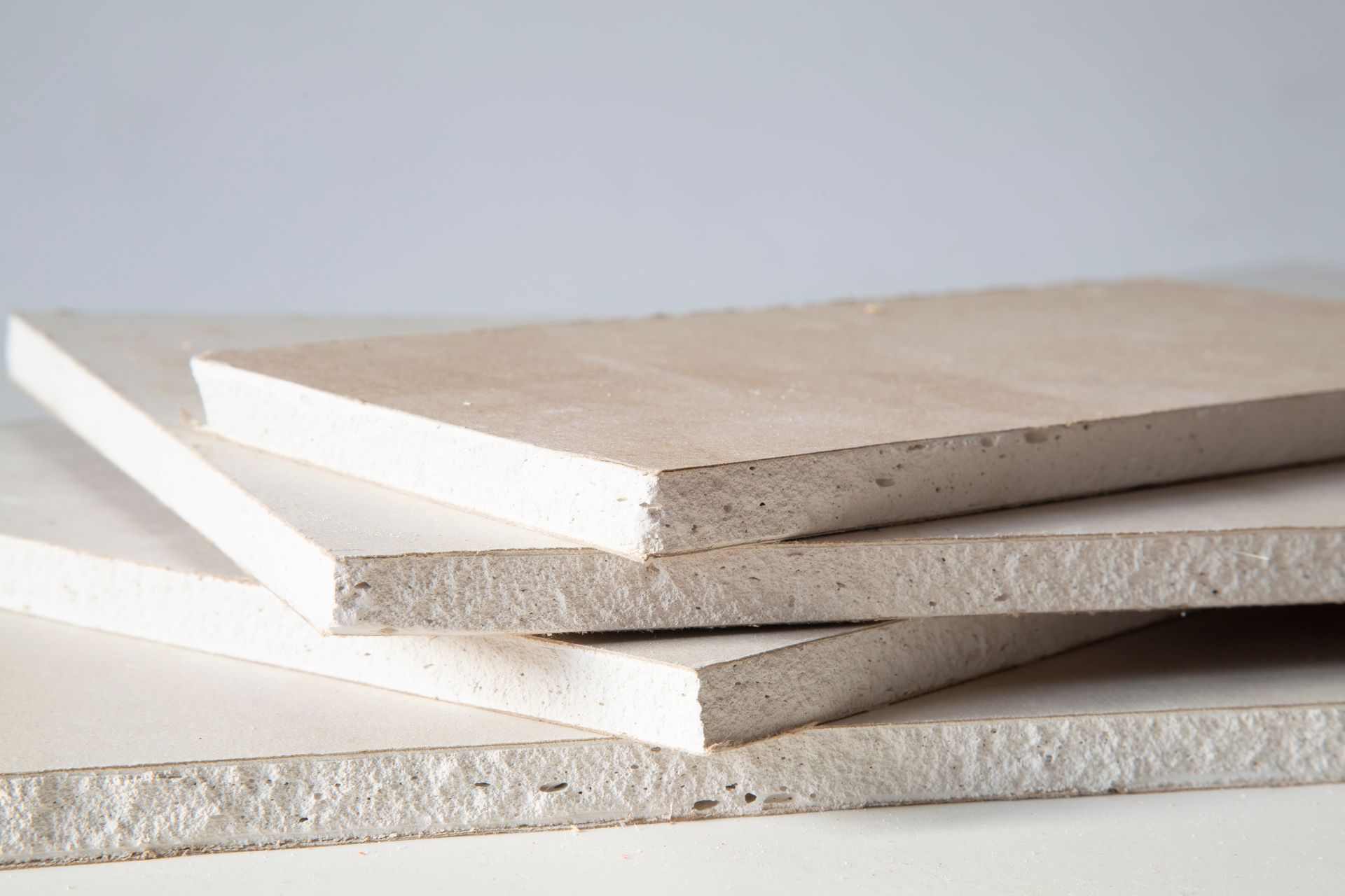 Stack of drywall panels with exposed edges on a light surface.