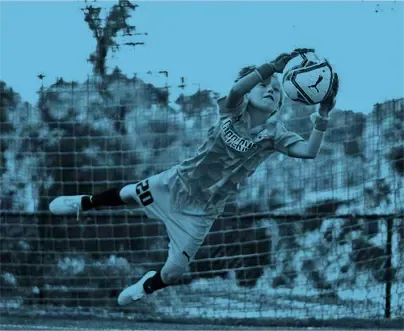 a soccer goalie is jumping in the air to catch a soccer ball .