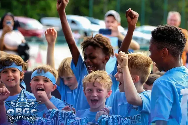 a group of Coppermine Soccer Club young boys in blue shirts are raising their arms in the air after winning obgc cup.