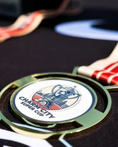 Close-up of a medal with a Super City Charity logo on a red-and-white ribbon.