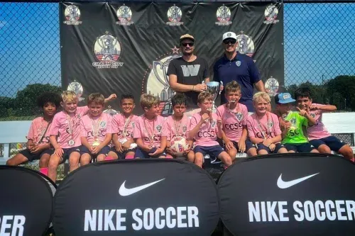 Youth soccer team posing with coaches behind Nike Soccer barriers on a sunny field.