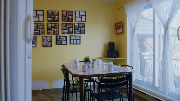 Salle à manger jaune avec une table mise pour le repas. Cadres photo au mur, fenêtre avec rideaux blancs.