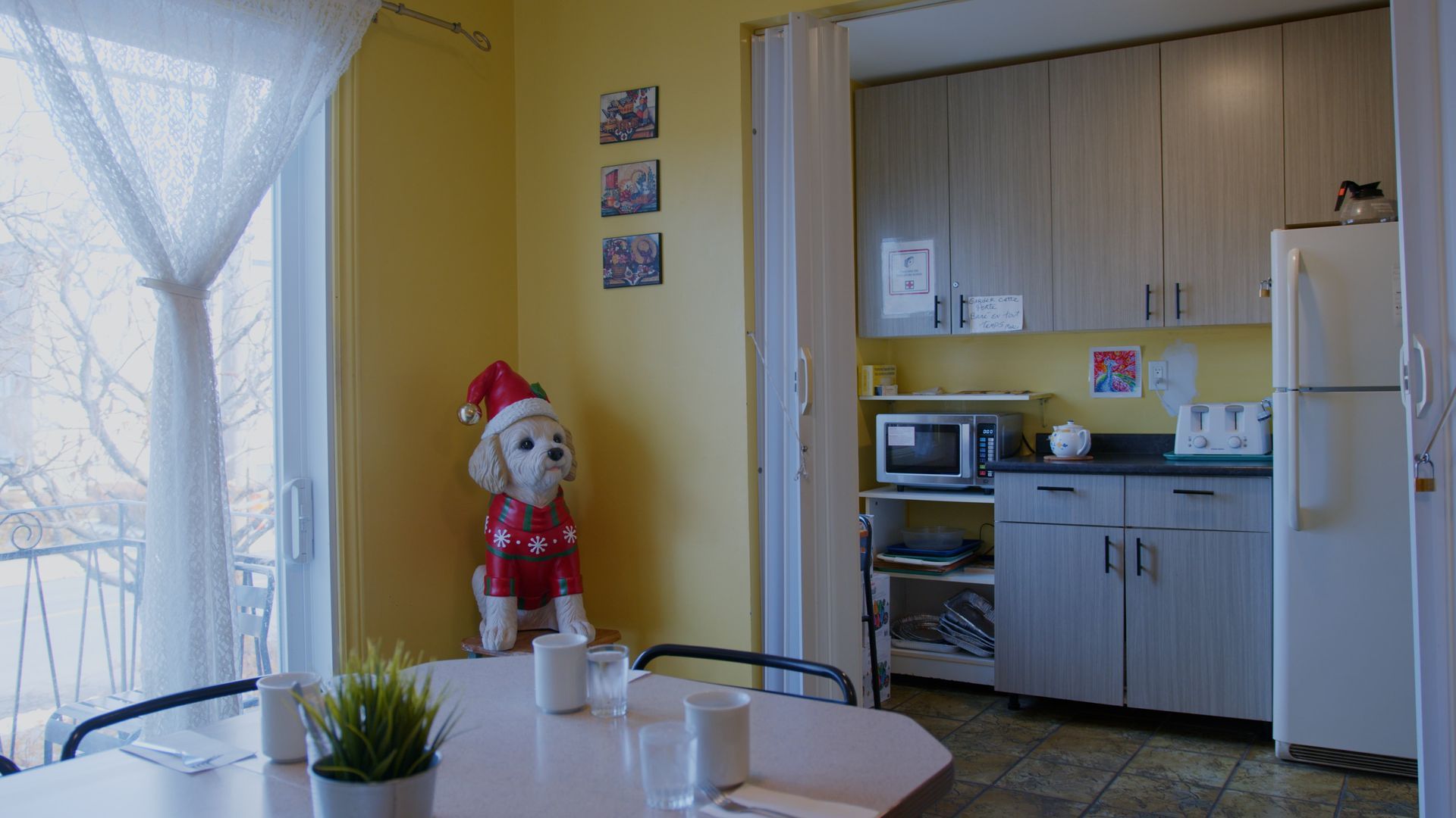 Cuisine chaleureuse avec coin repas, une statue de chien de Noël et une vue depuis un balcon à travers une fenêtre.