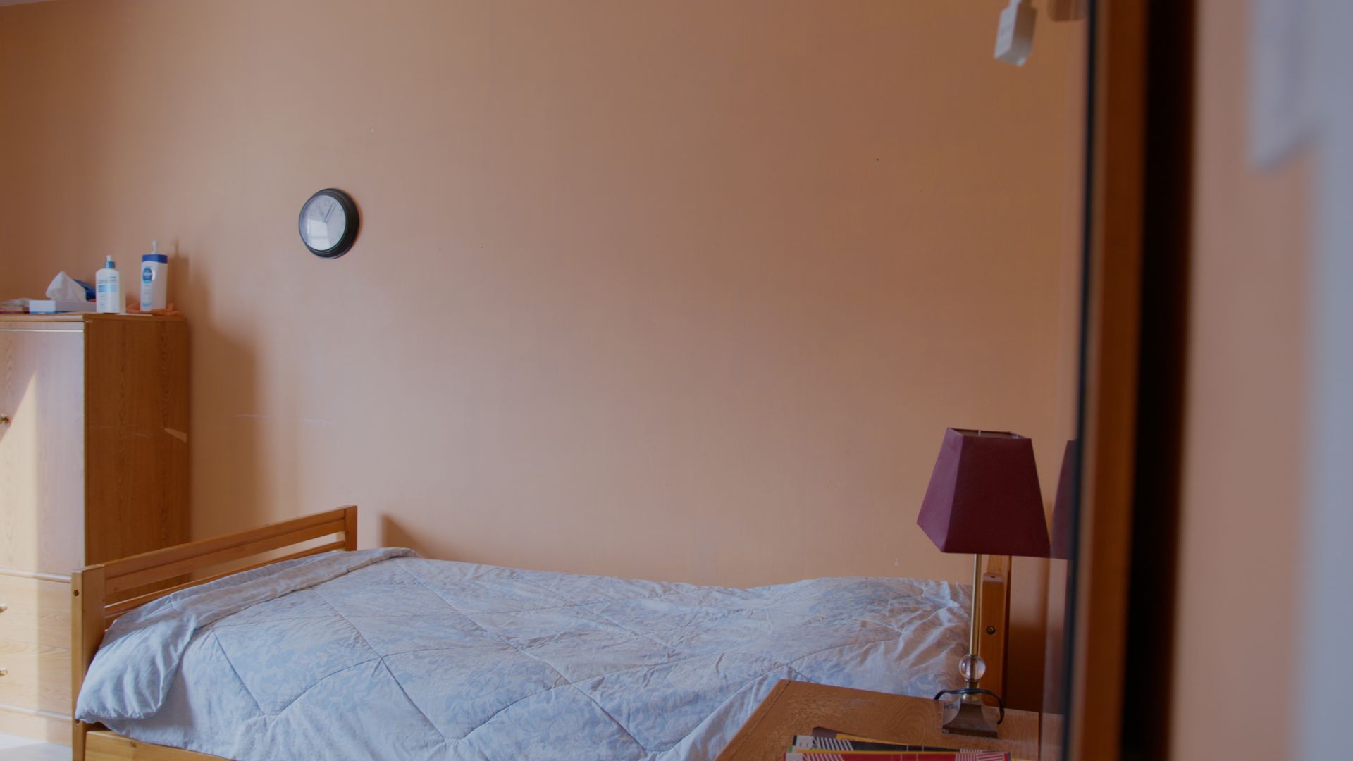 Chambre avec un lit, une table de chevet, une lampe et une horloge sur un mur peint en orange.