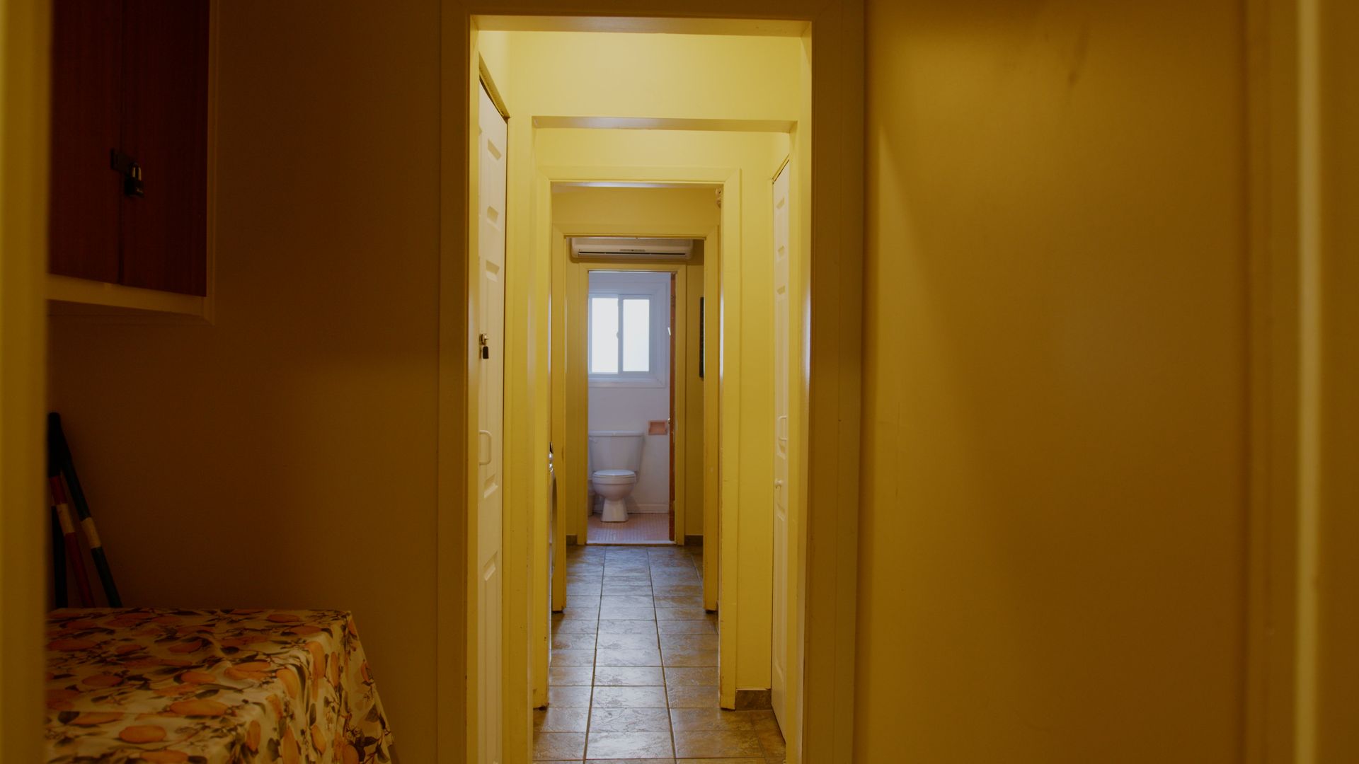 Couloir étroit avec des portes et une salle de bains visible au fond ; éclairage chaleureux.