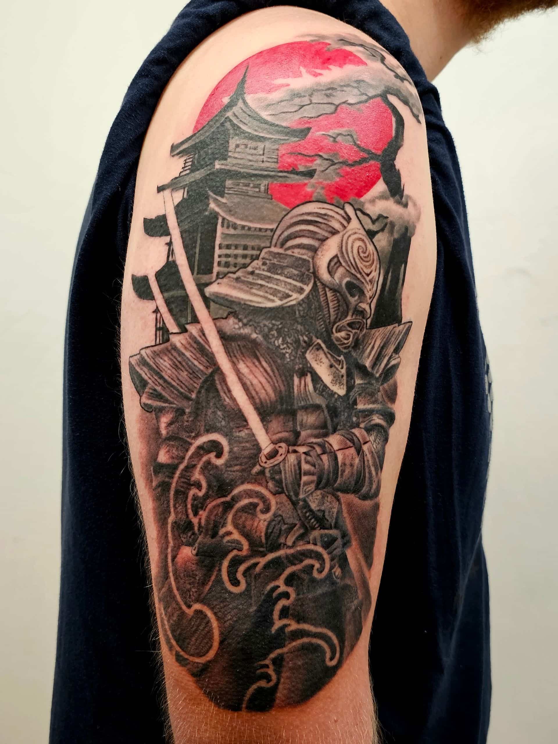 A tattoo on an upper arm featuring a samurai holding a sword, a traditional Japanese building, and a bright red sun.