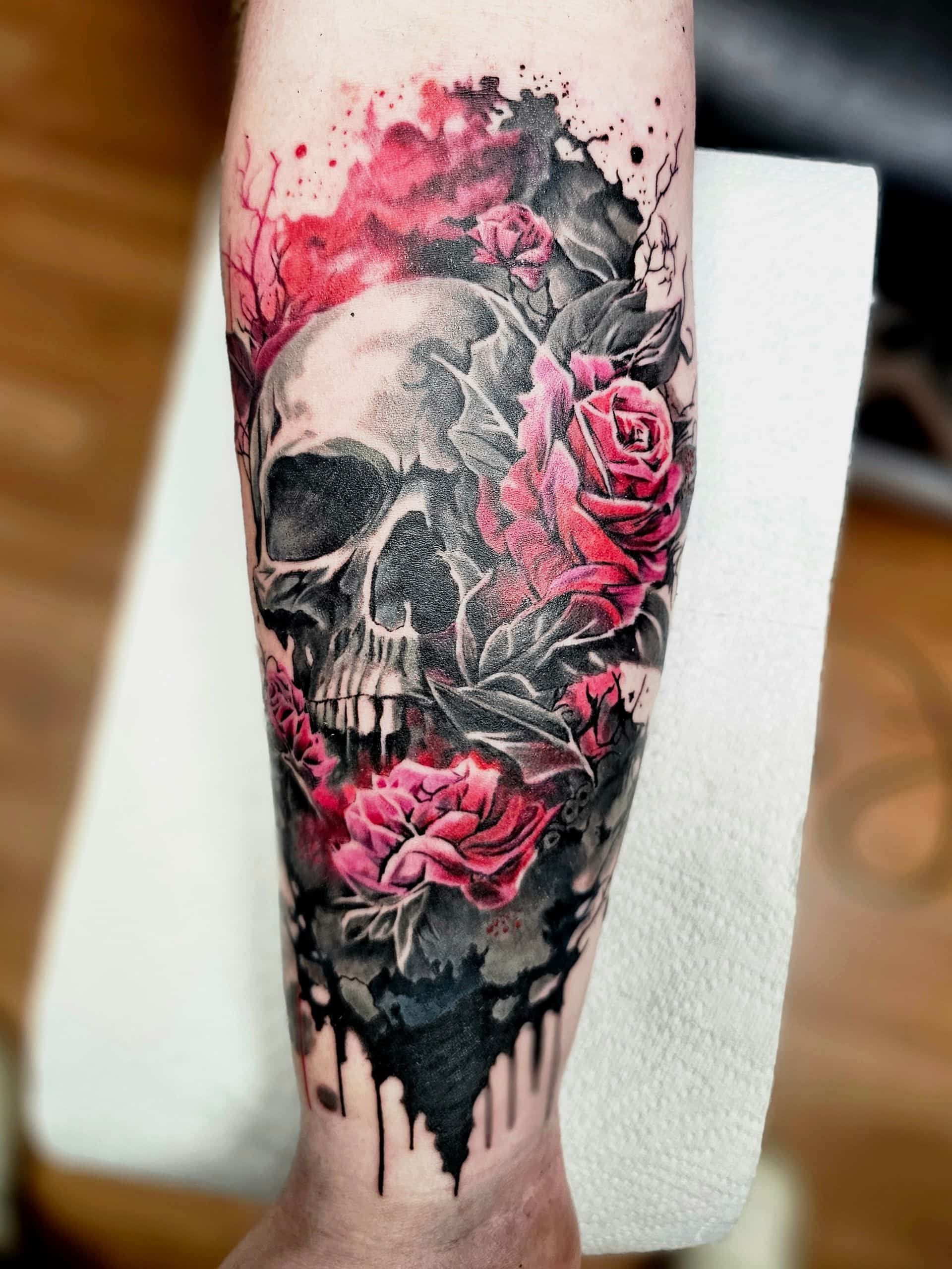 Tattoo of a realistic human skull intertwined with vibrant pink roses and dramatic black ink splatter on an arm.