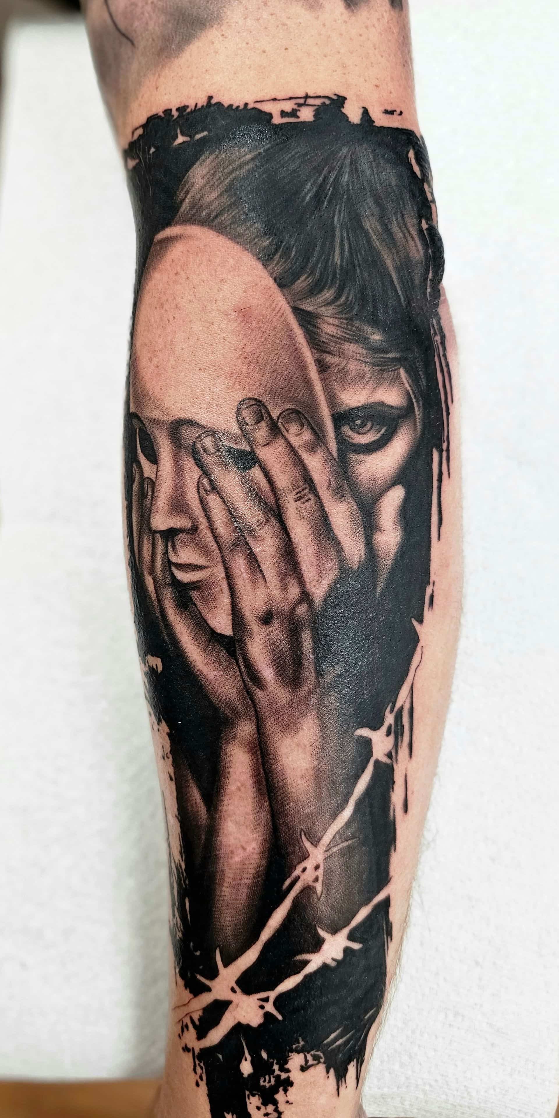 A black-and-grey tattoo of a person holding a featureless mask over their face, framed by barbed wire and dark ink.