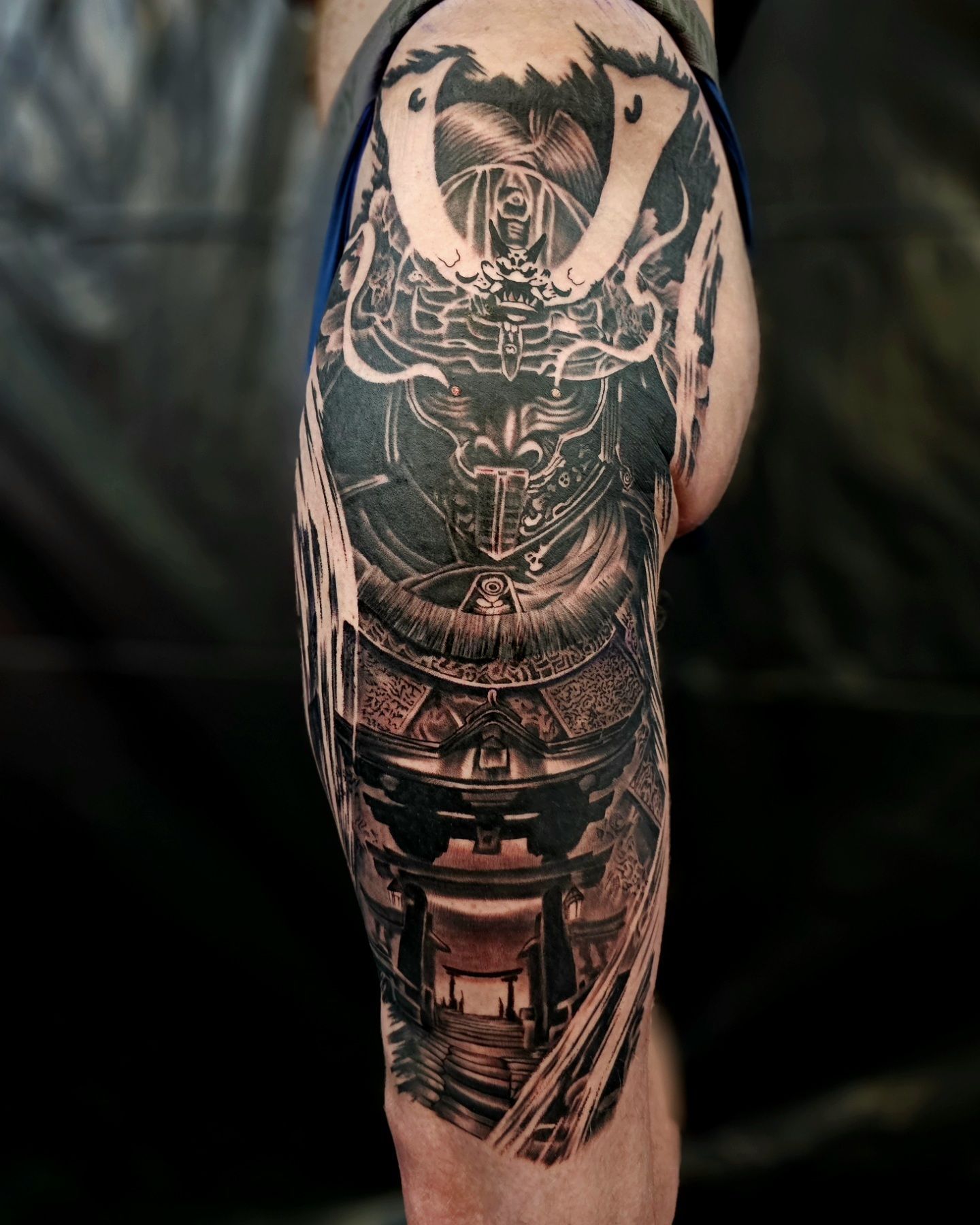 Detailed black and grey tattoo of a samurai helmet and armor on a person's thigh, featuring intricate Japanese patterns.