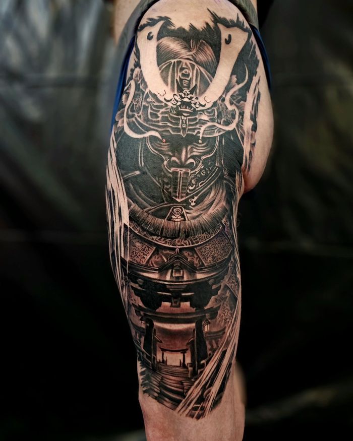 A detailed black and grey tattoo on a person's thigh depicting a samurai helmet, armor, and a traditional torii gate.