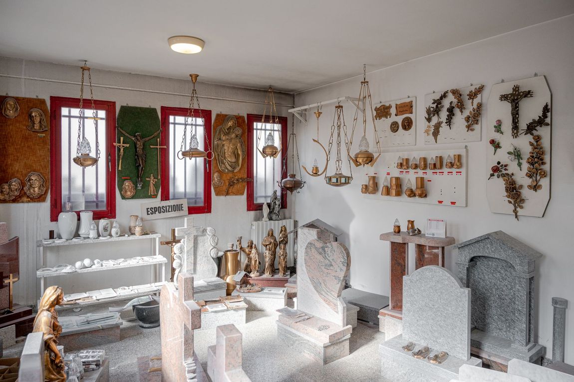 Uno showroom ricco di monumenti in pietra, croci e sculture religiose esposte contro vetrine luminose.